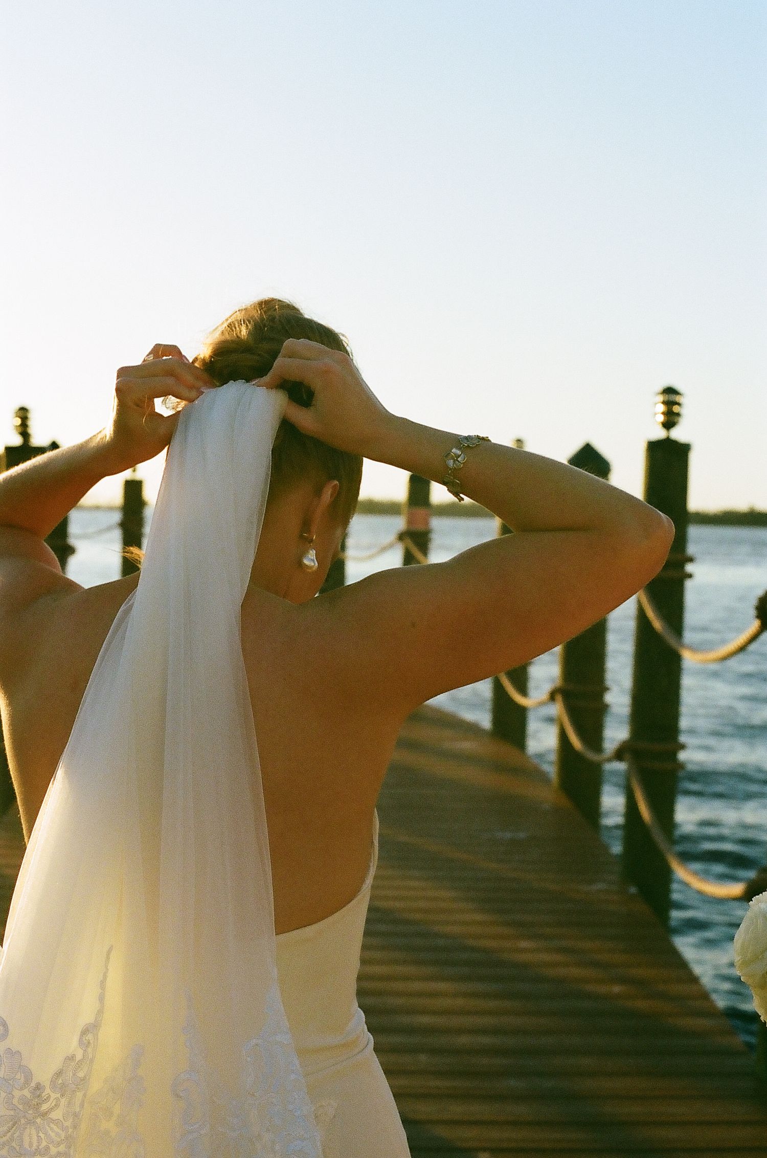 White wedding veil flowing in the breeze against a waterfront dock at sunset.