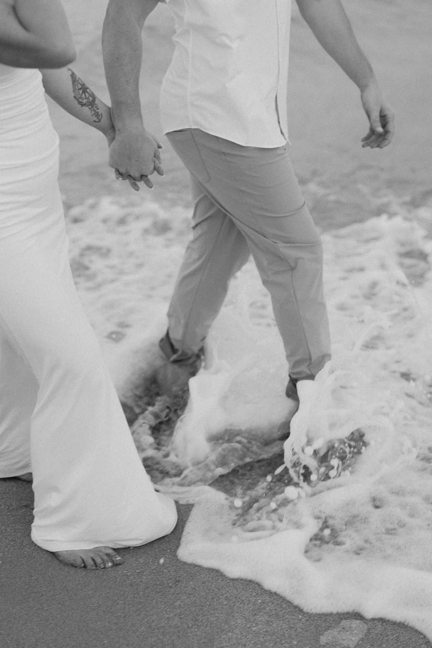Close-up of feet in the sand as ocean waves wash over them during a beach photoshoot.