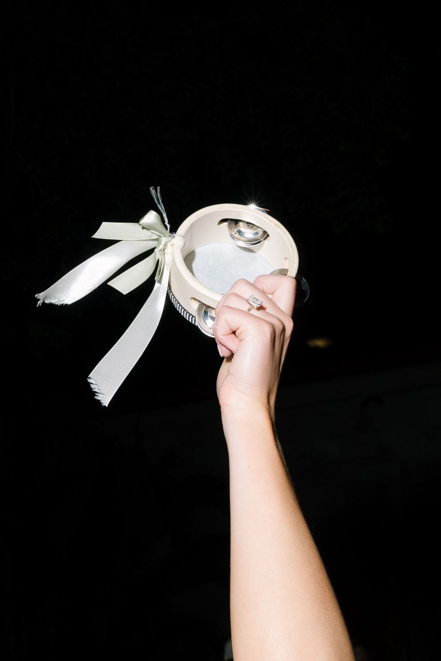 Bride holding decorative wedding accessory with ribbon bow and engagement ring visible on hand.