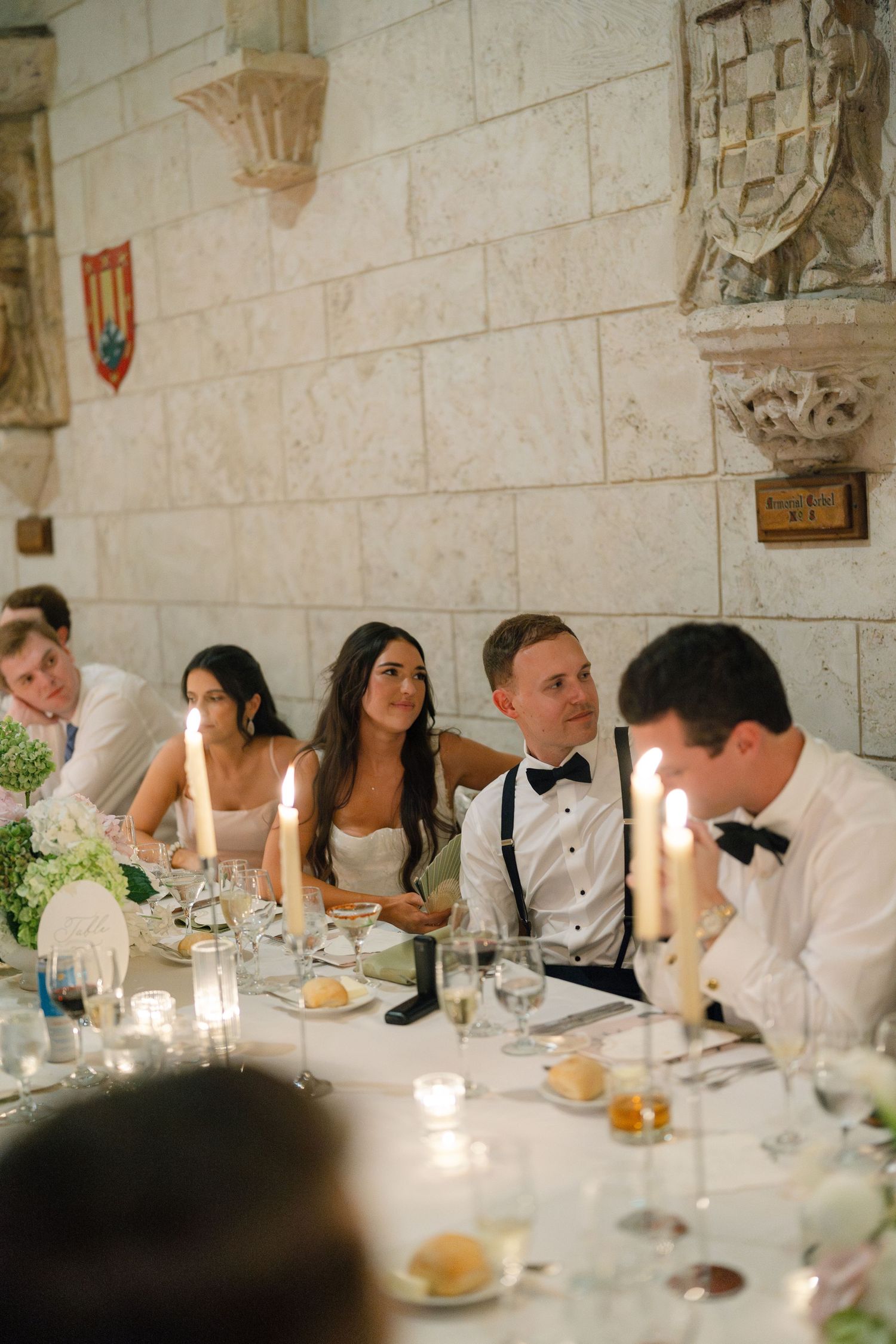 Bride and groom seated at candlelit wedding reception table in elegant stone-walled venue.