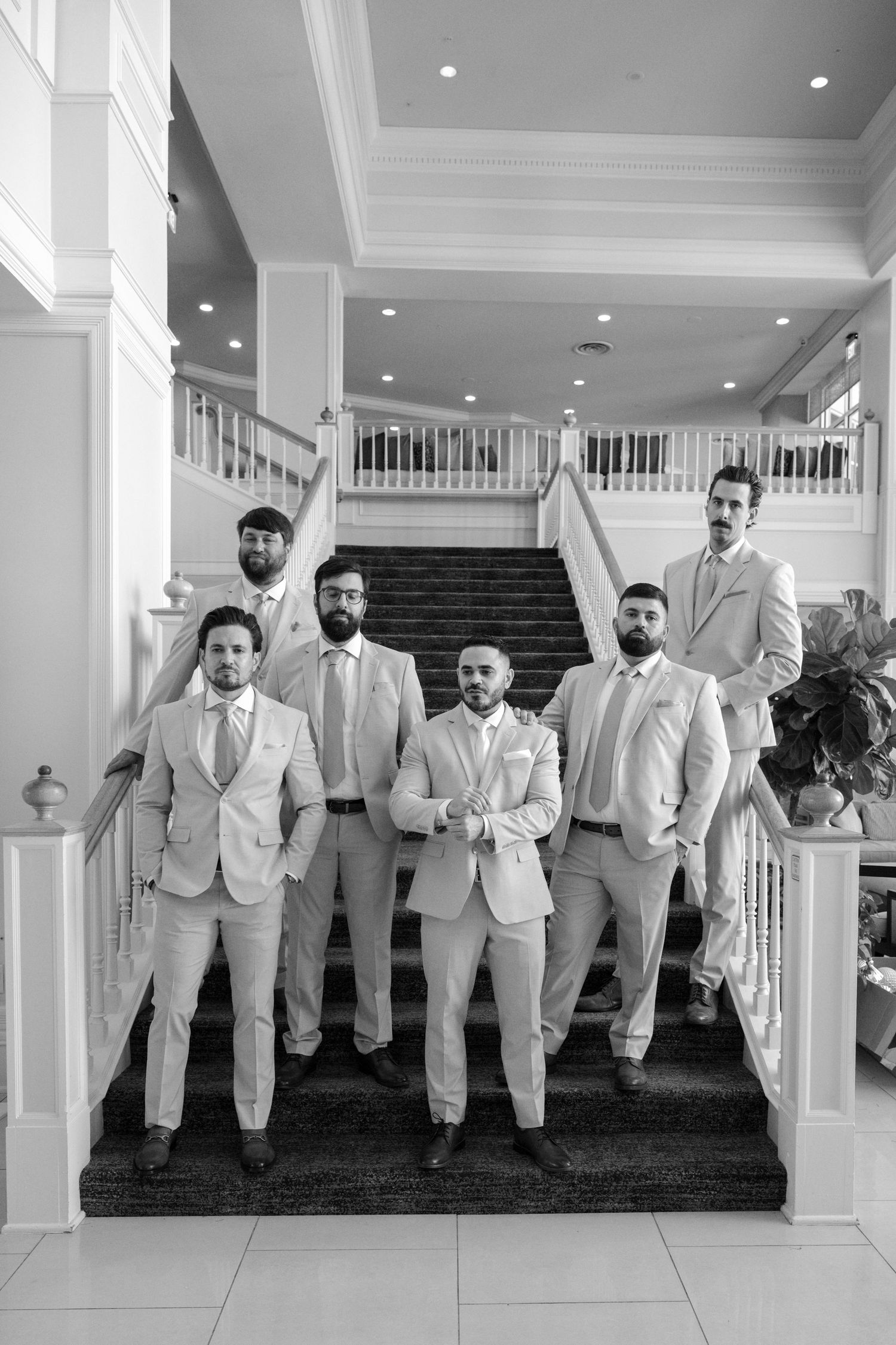 Wedding party in matching light suits posing on grand staircase.