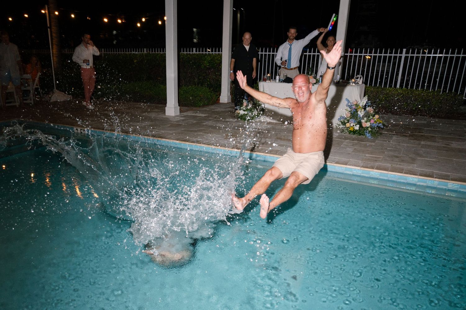 Person making a splash jumping into a pool during nighttime celebration.