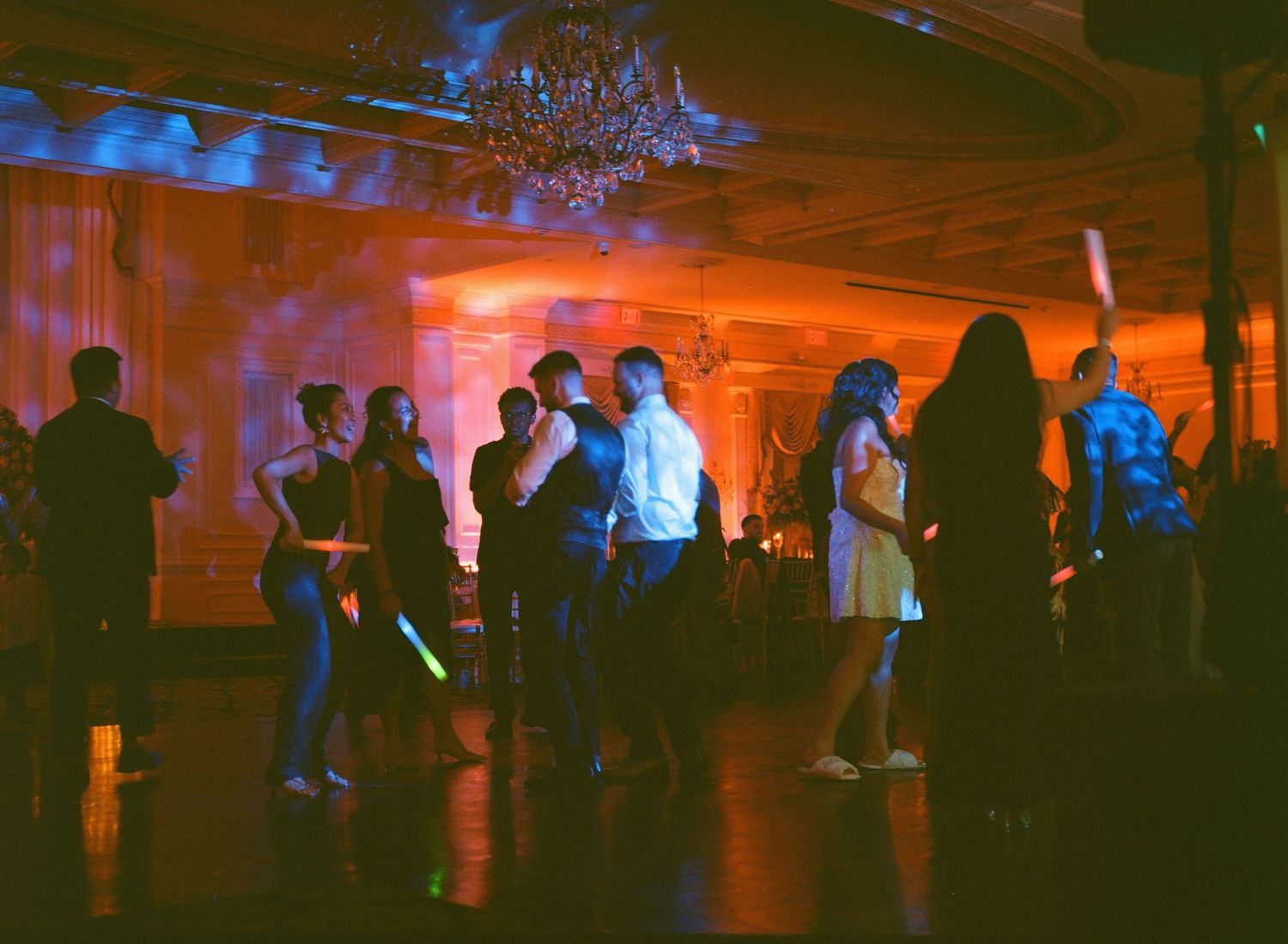 Silhouettes of wedding guests dancing in a reception venue with dramatic orange and blue lighting.