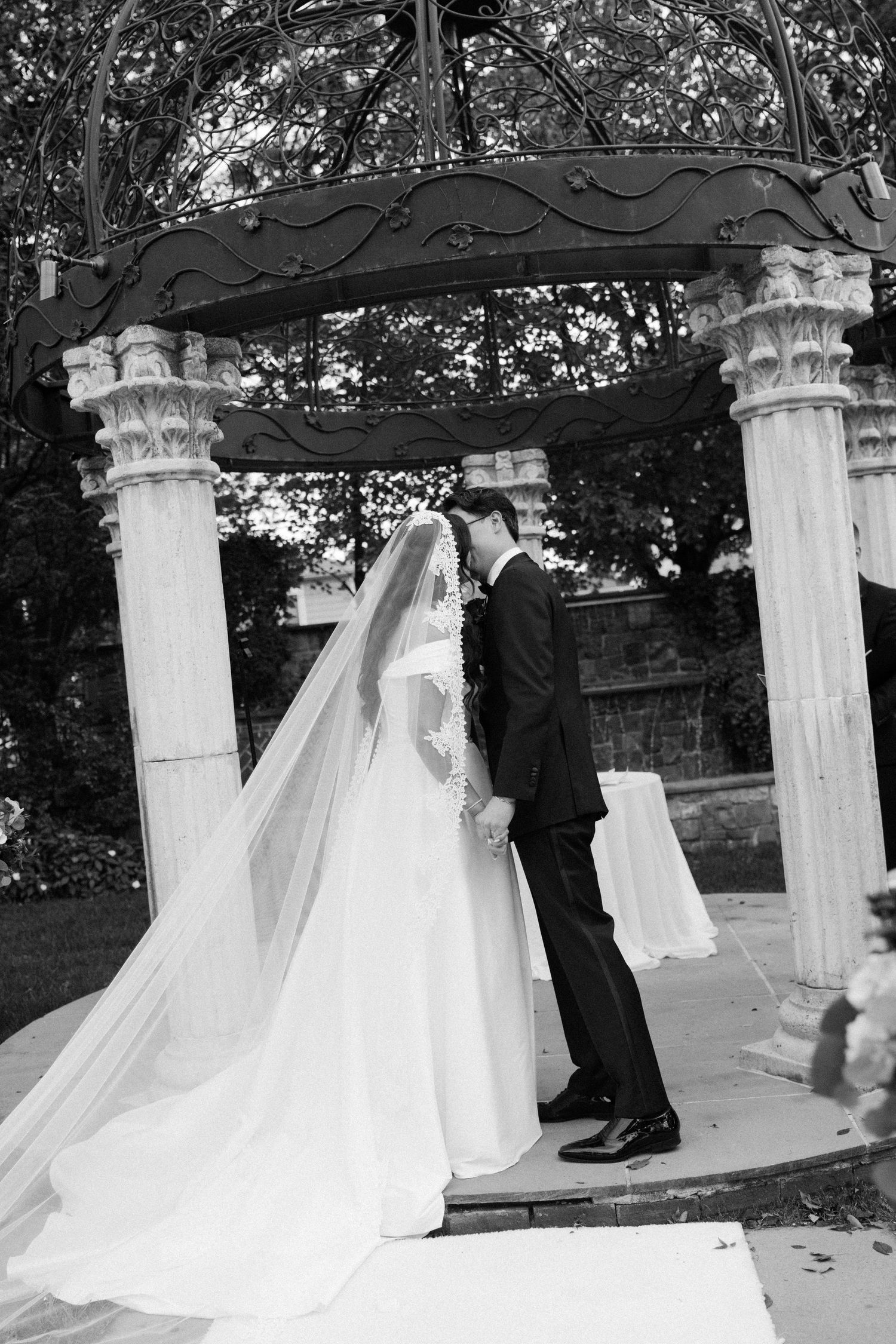 Black and white wedding ceremony photos under ornate stone gazebo with dramatic veil.