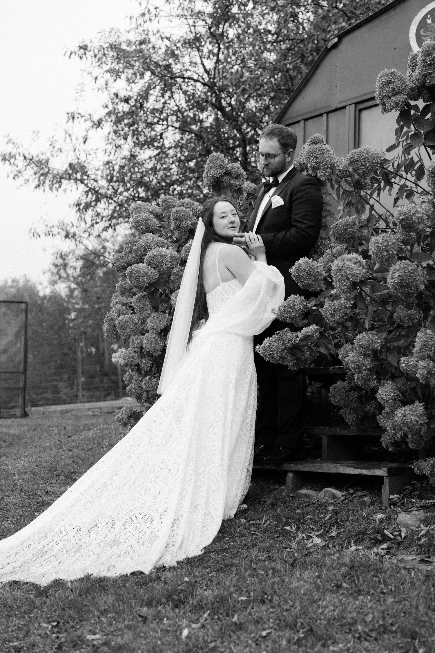 Newlyweds share a romantic dance moment in a garden setting with blooming trees in the background.