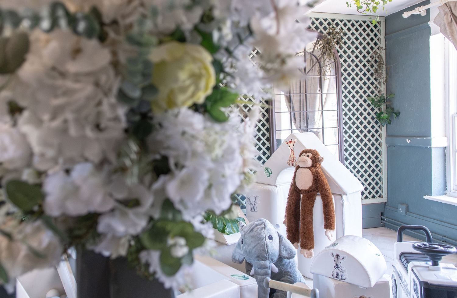 Elegant nursery decor with white floral arrangements and stuffed animal toys on a white dresser.