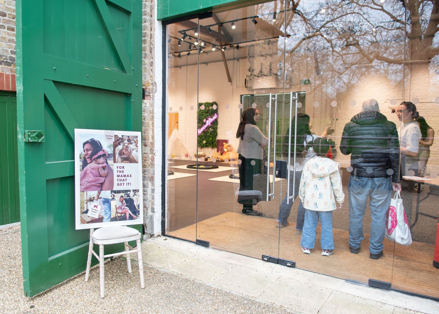 People browsing a bright art gallery shop with green doors and a promotional poster display outside.