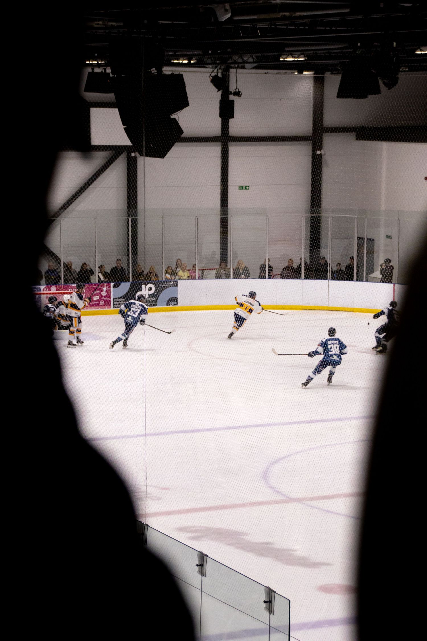 Hockey game viewed through arena equipment showing players on ice below.