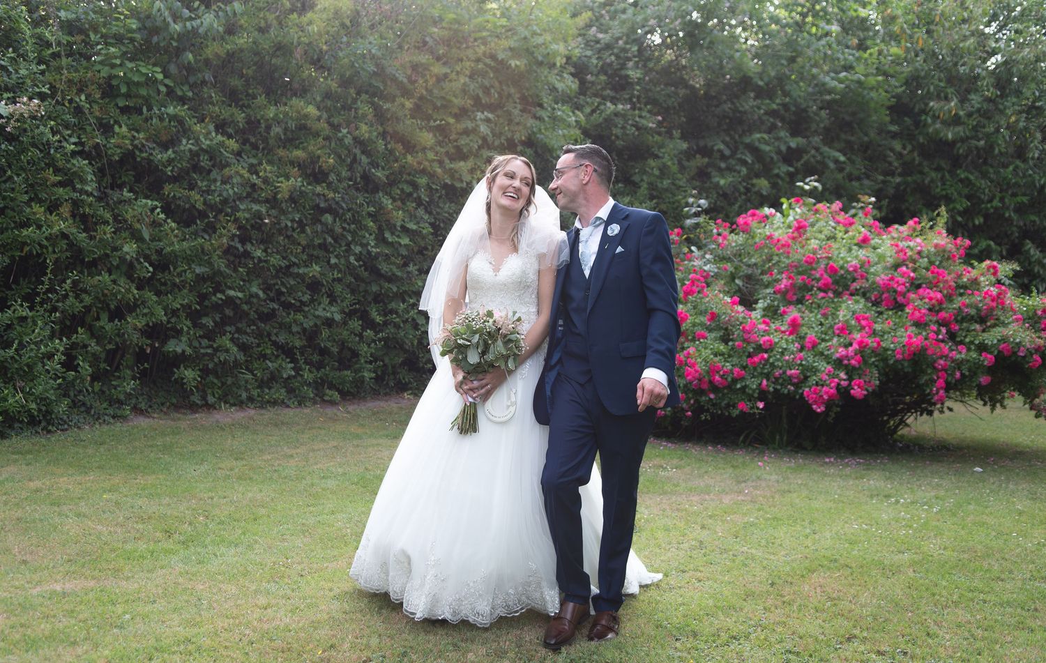 Bride and groom sharing a romantic moment in a garden with blooming pink roses.