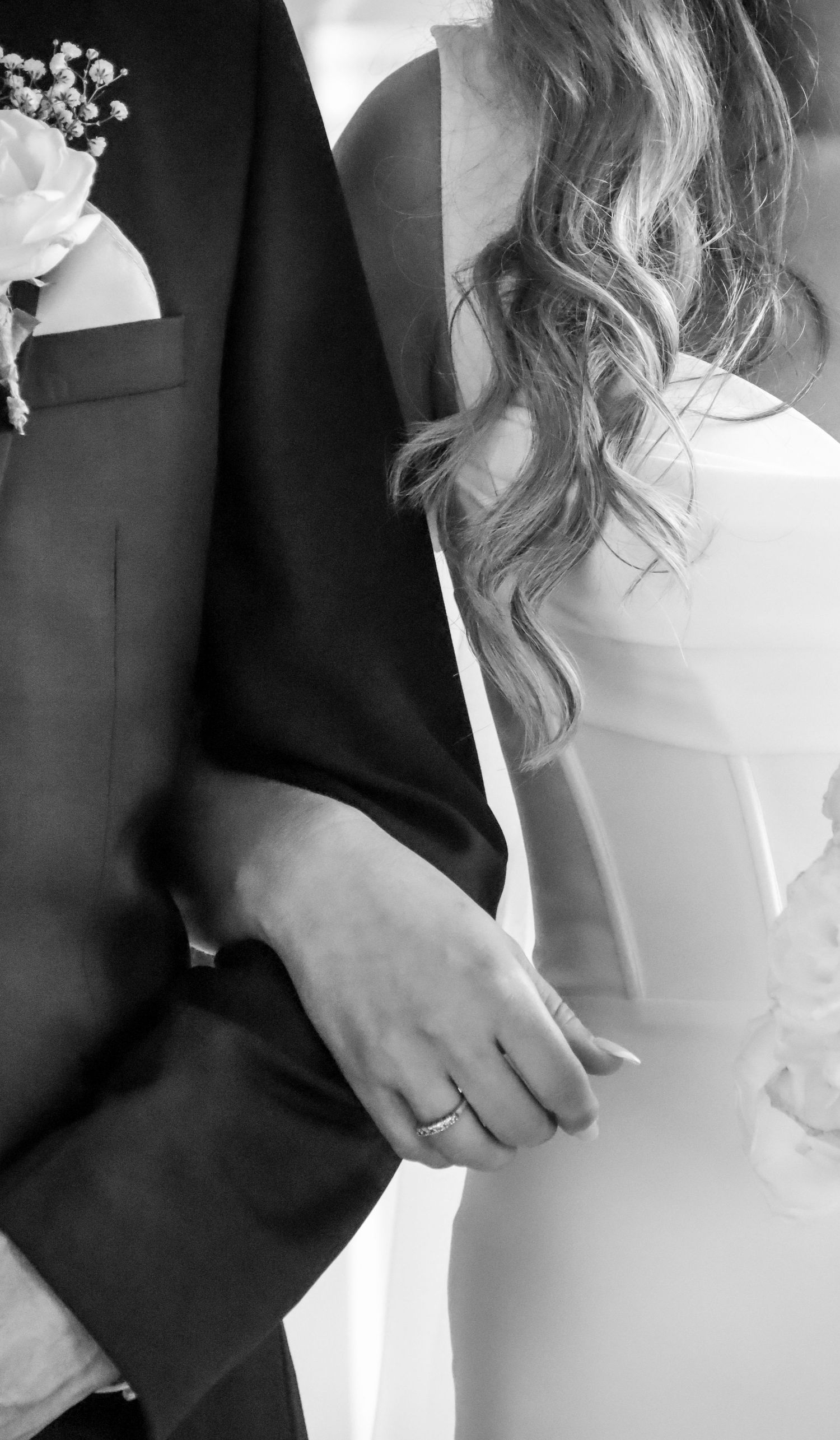 Close-up black and white details of formal wedding attire and hands.