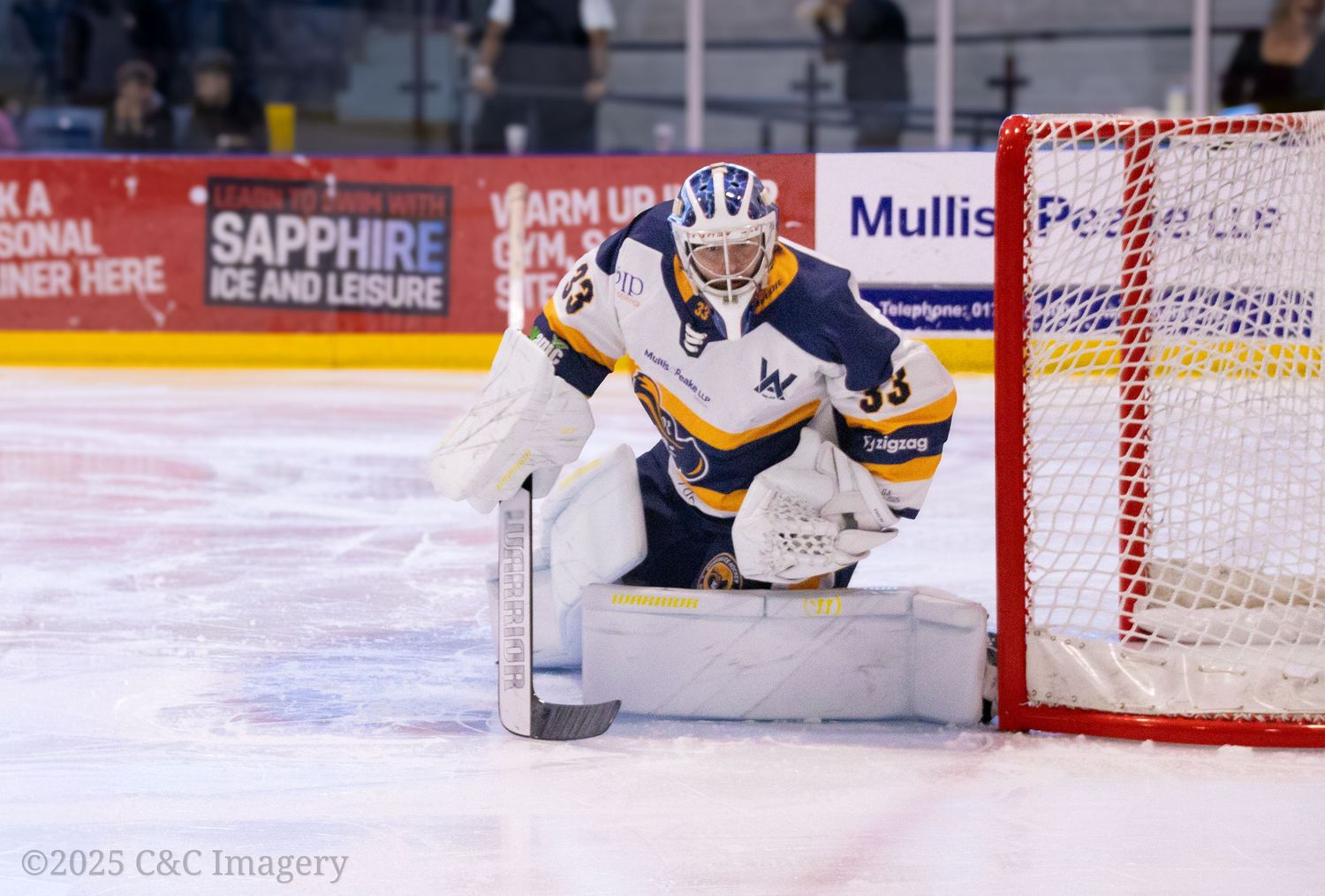 Hockey puck sliding across ice towards red goal net during game action.