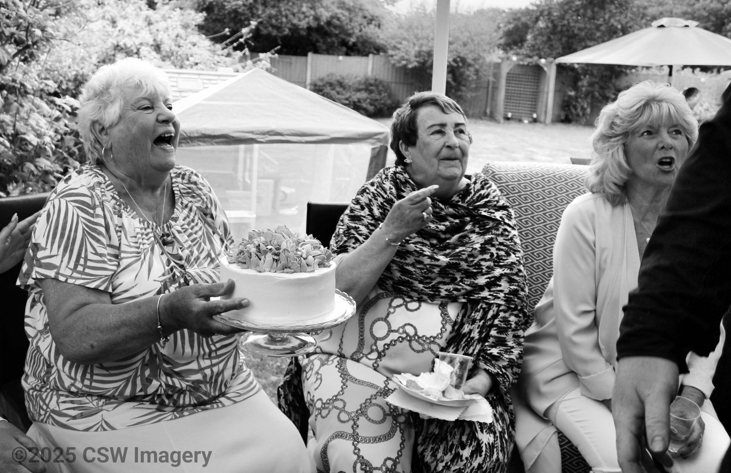 Three women laugh together while enjoying themselves at an outdoor social gathering.