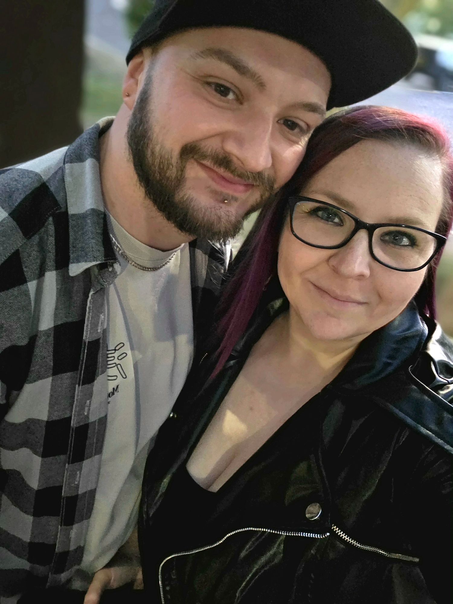 A couple poses for selfies in a car wearing casual winter clothing.