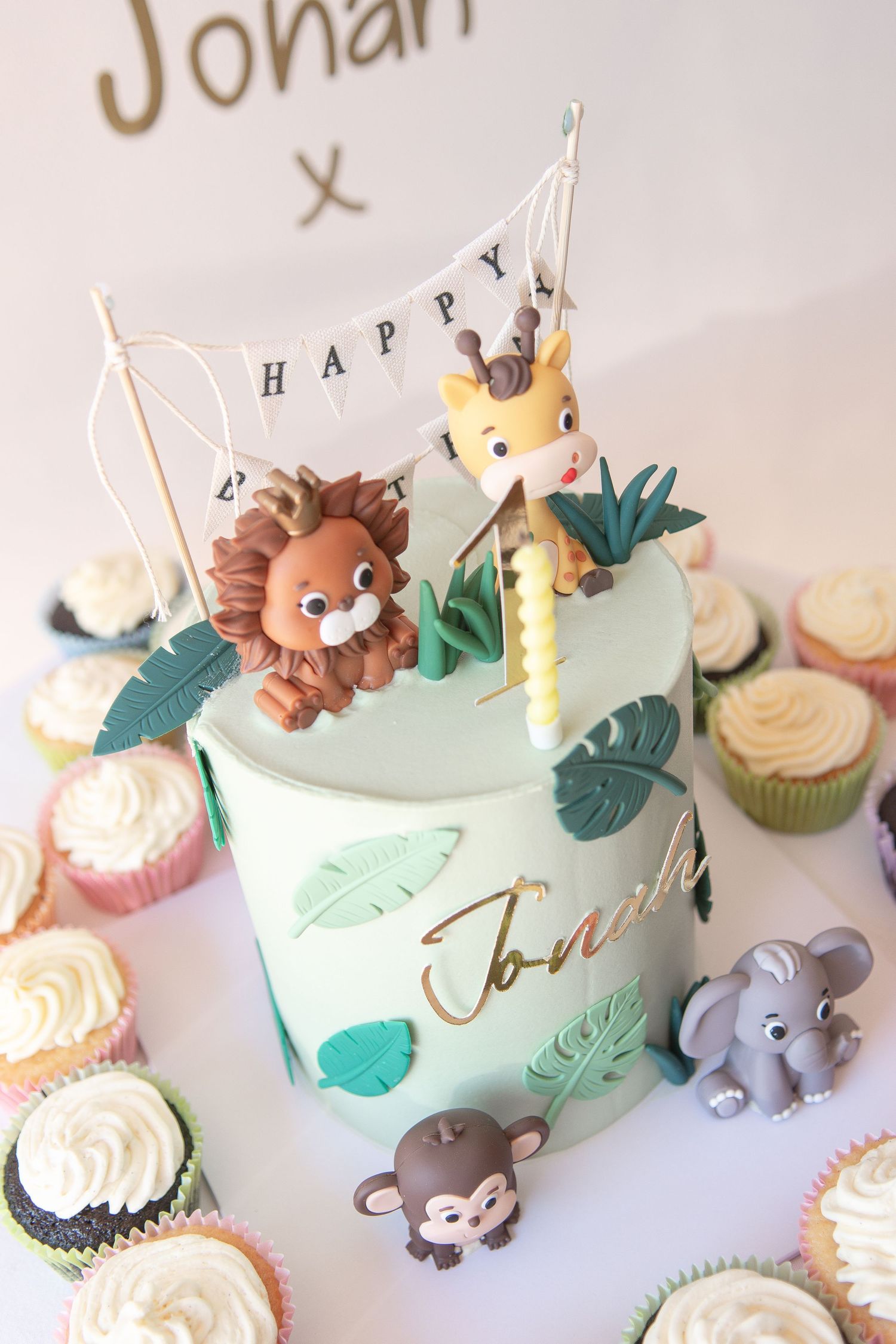 Safari-themed birthday cake with lion and giraffe toppers, surrounded by cupcakes.
