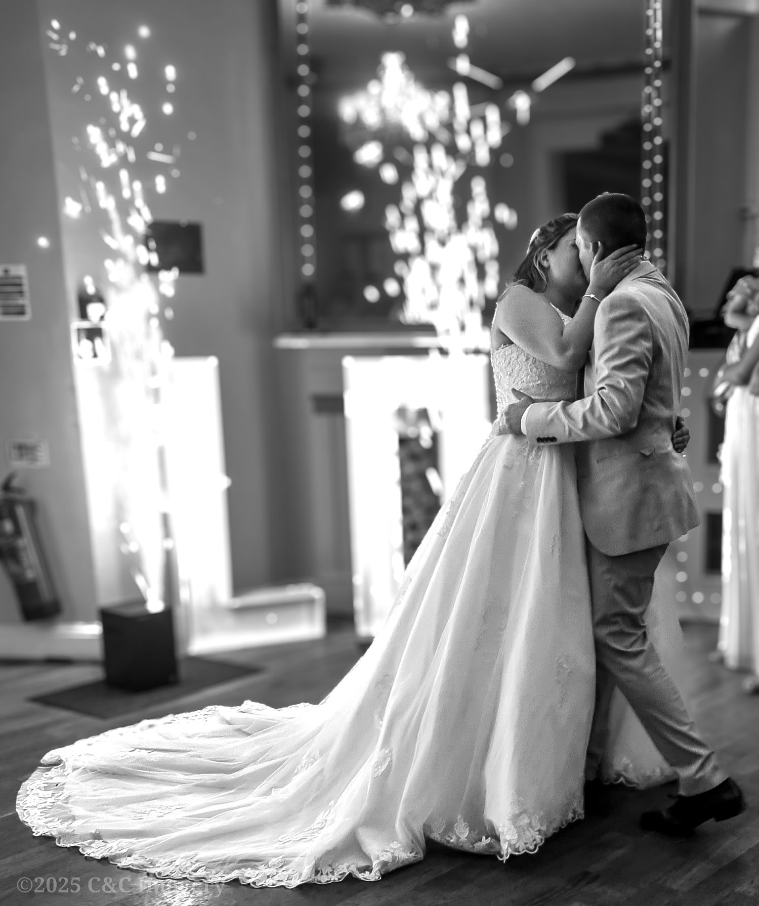 Silhouette of wedding dress train flowing on dark floor with sparkly lights in background.