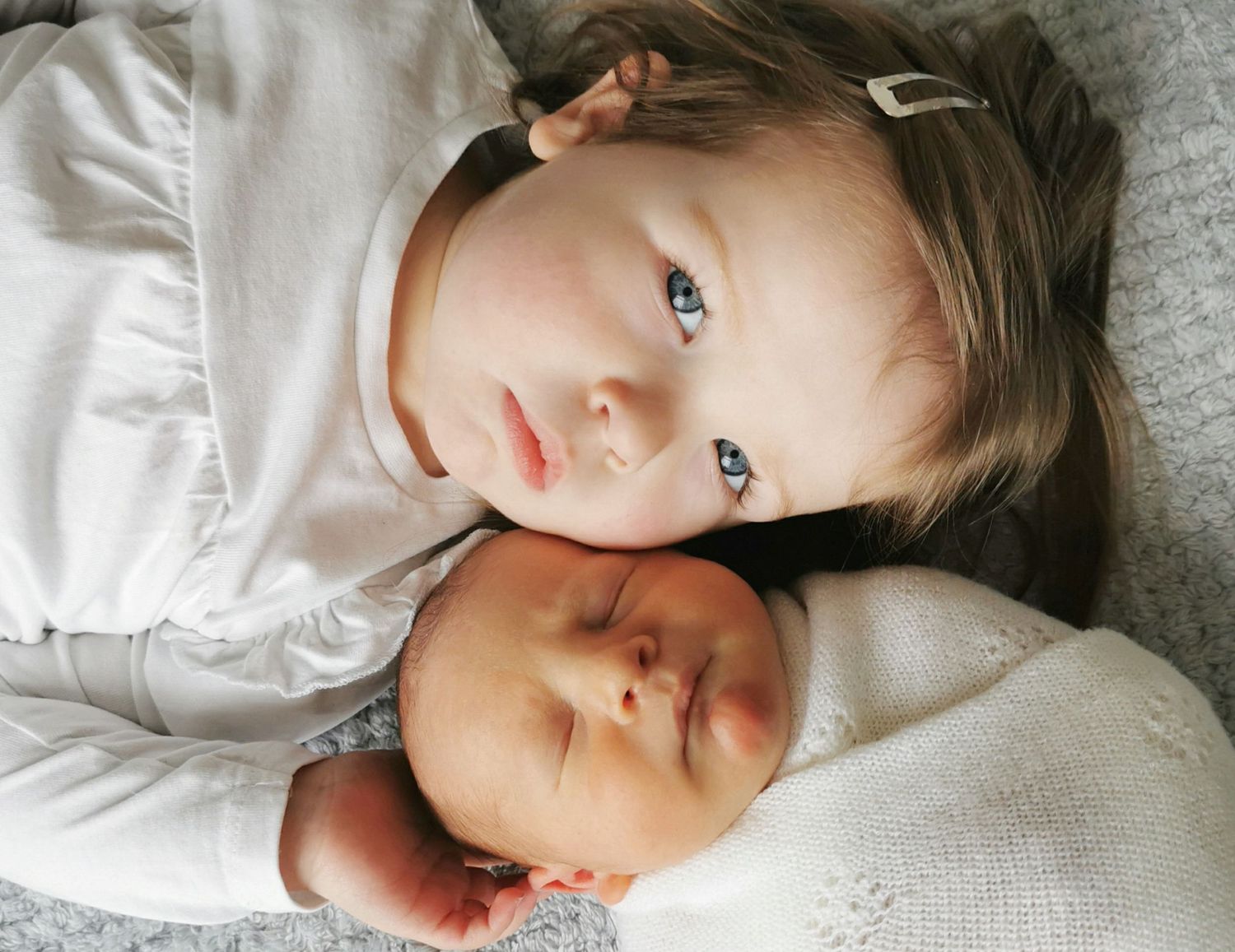 Siblings sharing a tender moment on soft white blankets.