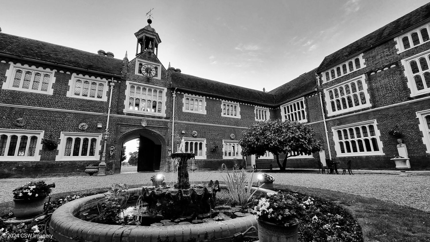 Black and white panoramic view of a historic brick school building with clock tower.