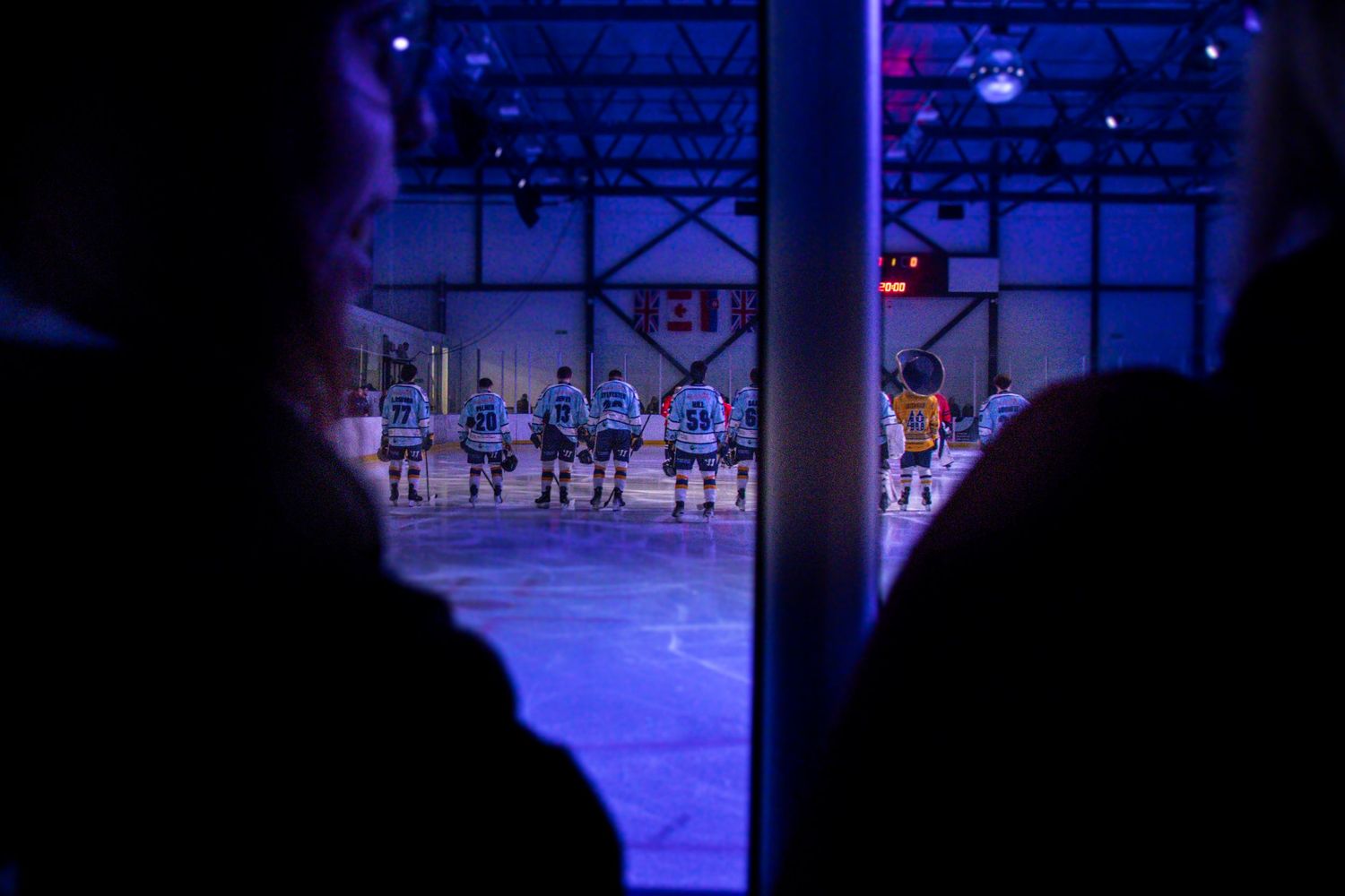 Hockey players on an illuminated ice rink with blue lighting creating a dramatic atmosphere during a game.