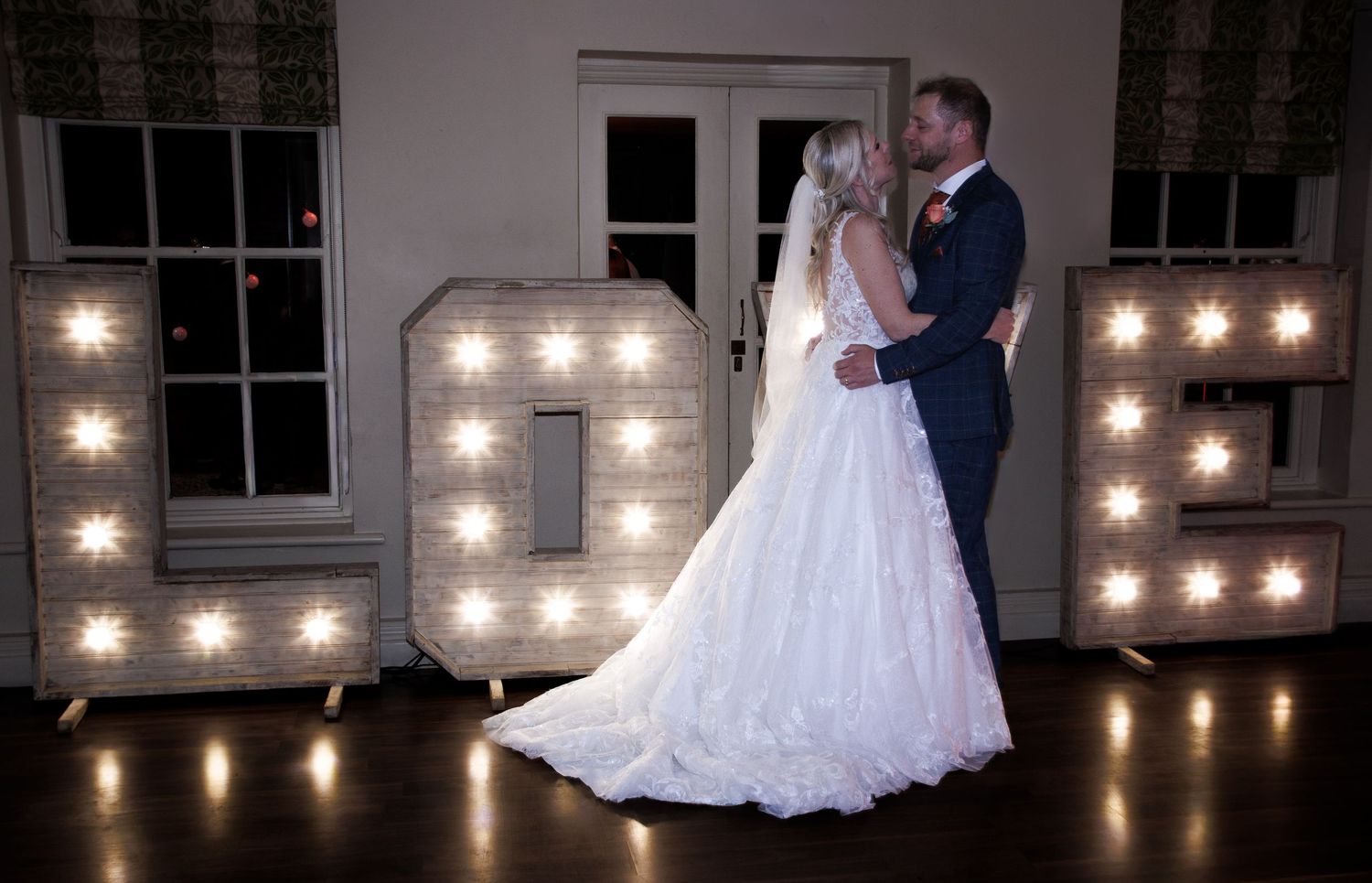 A romantic wedding couple dances in an elegant ballroom with glowing string lights creating a warm ambiance.