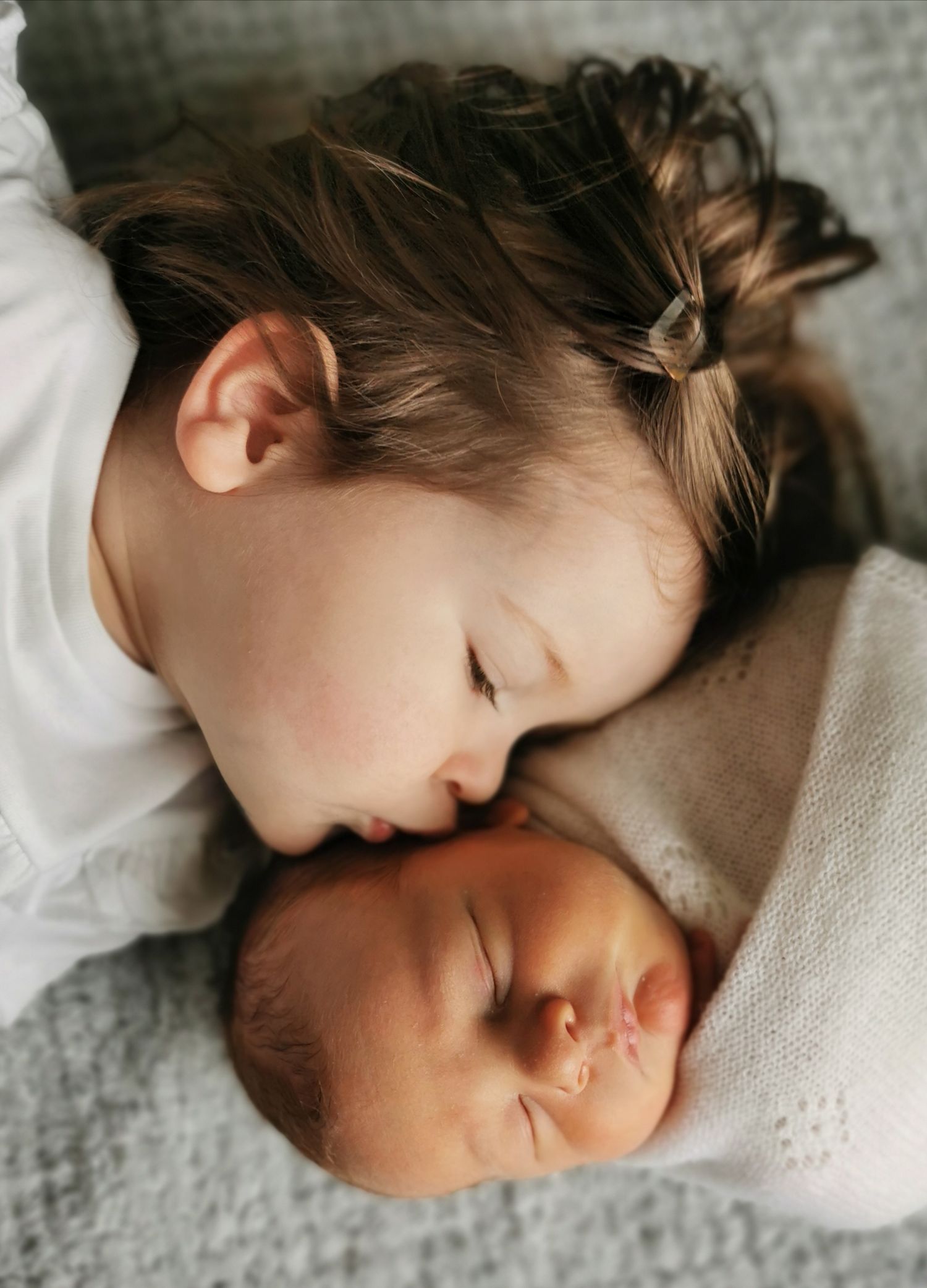 Children laying close together on a textured gray blanket.