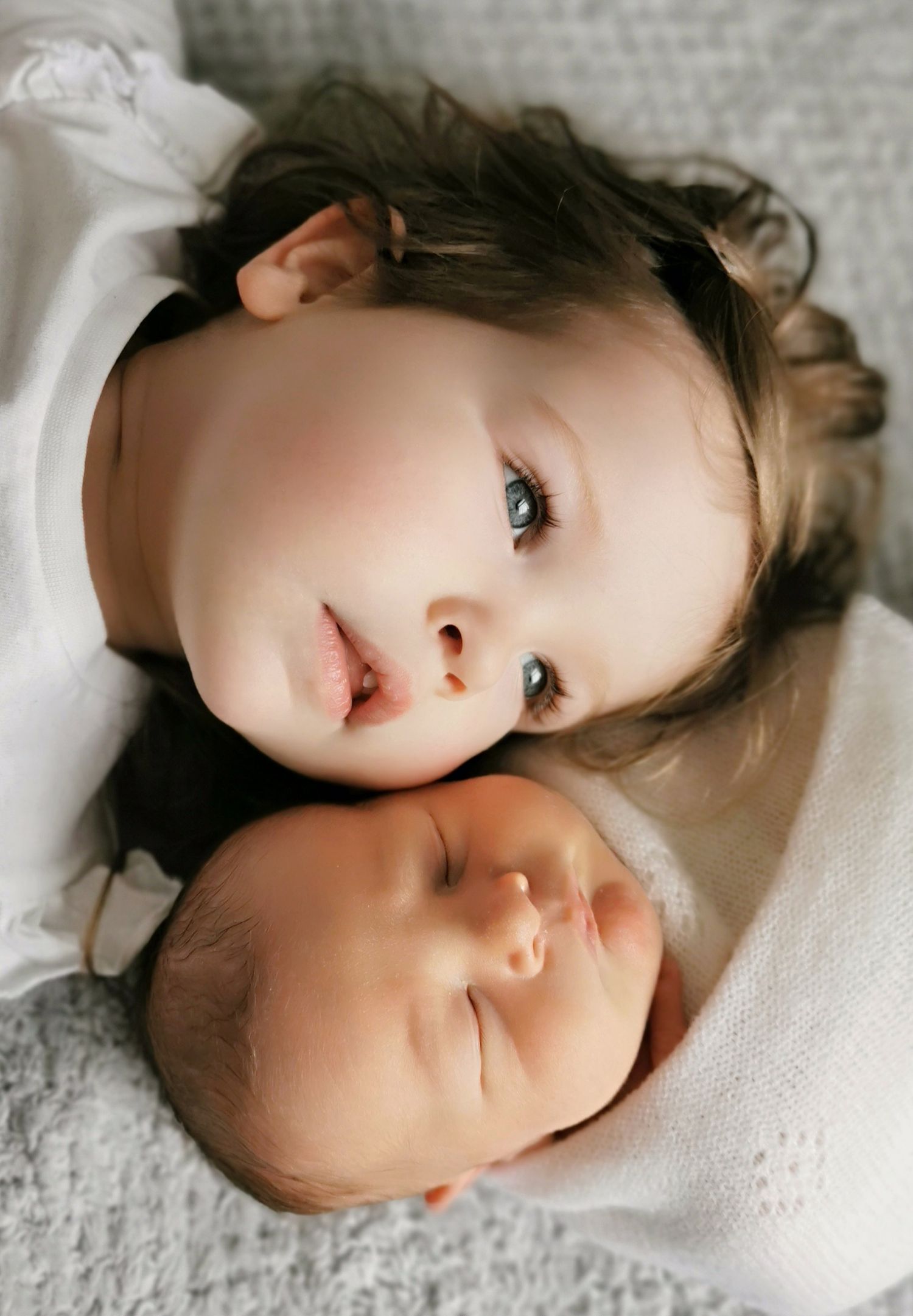 Two young children resting together on white bedding.