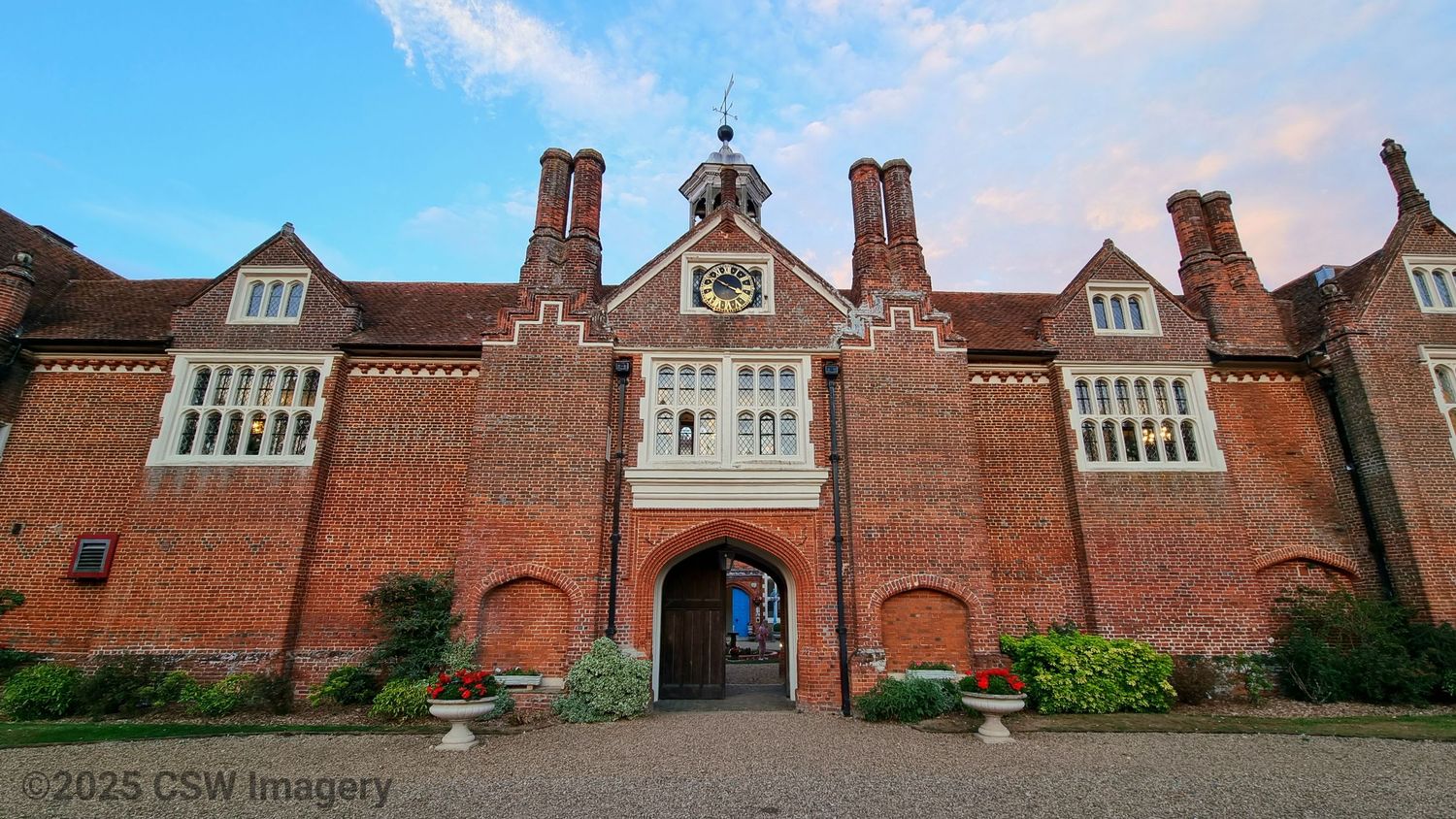 Panoramic view of a historic red brick building with Tudor-style architecture and arched entryway.