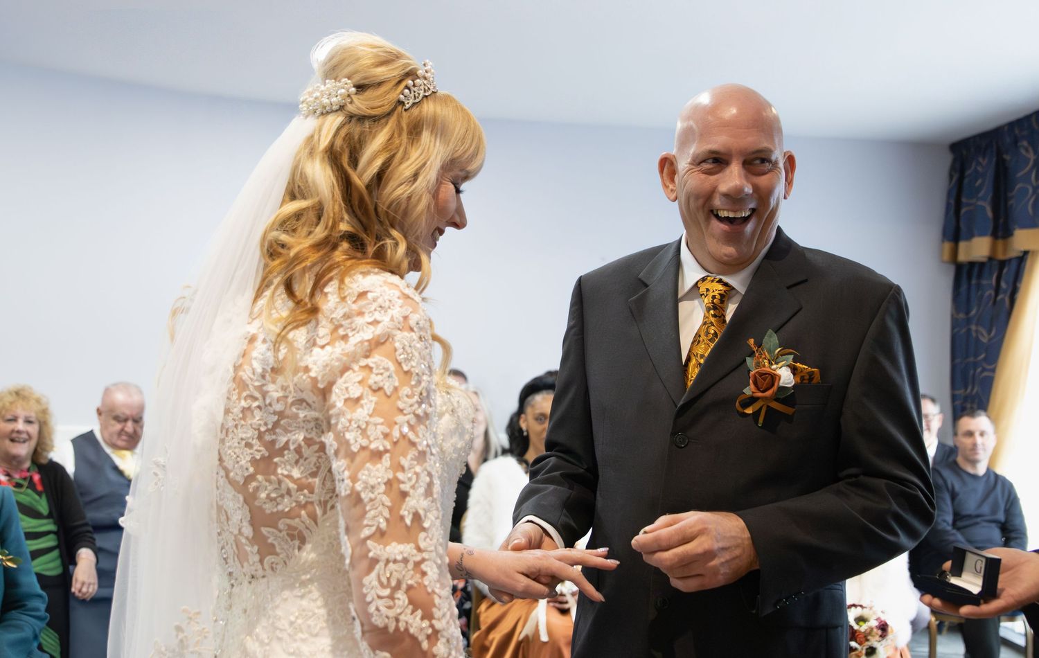 A couple exchanges rings during a wedding ceremony in a bright indoor setting.