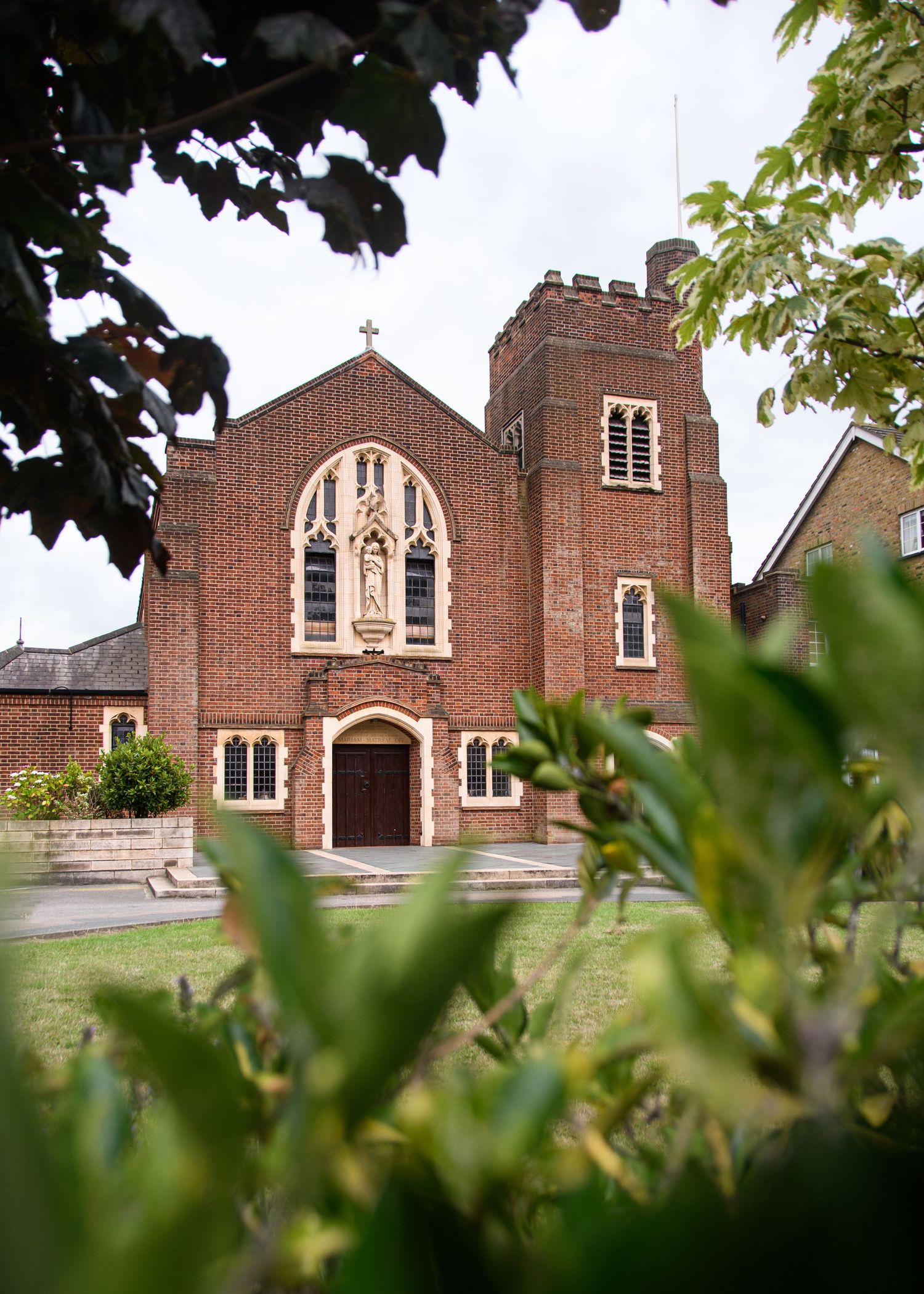 Red brick church exterior with Gothic windows and architectural details framed by trees.