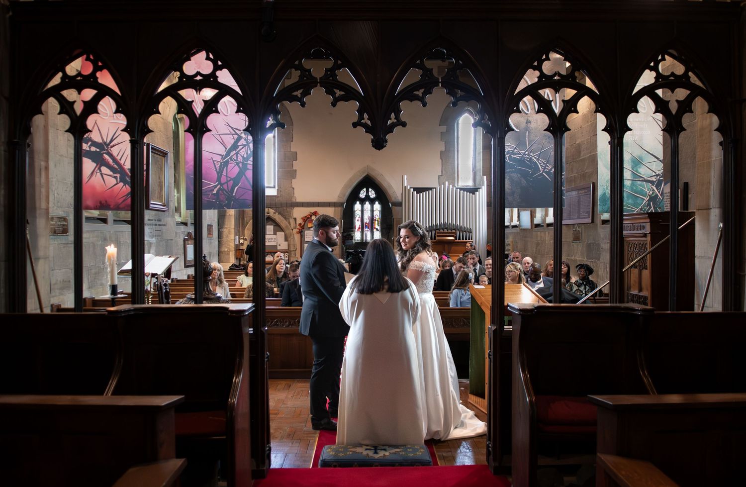 Bride and groom exchange vows at the altar of a stunning Gothic church with arched windows.