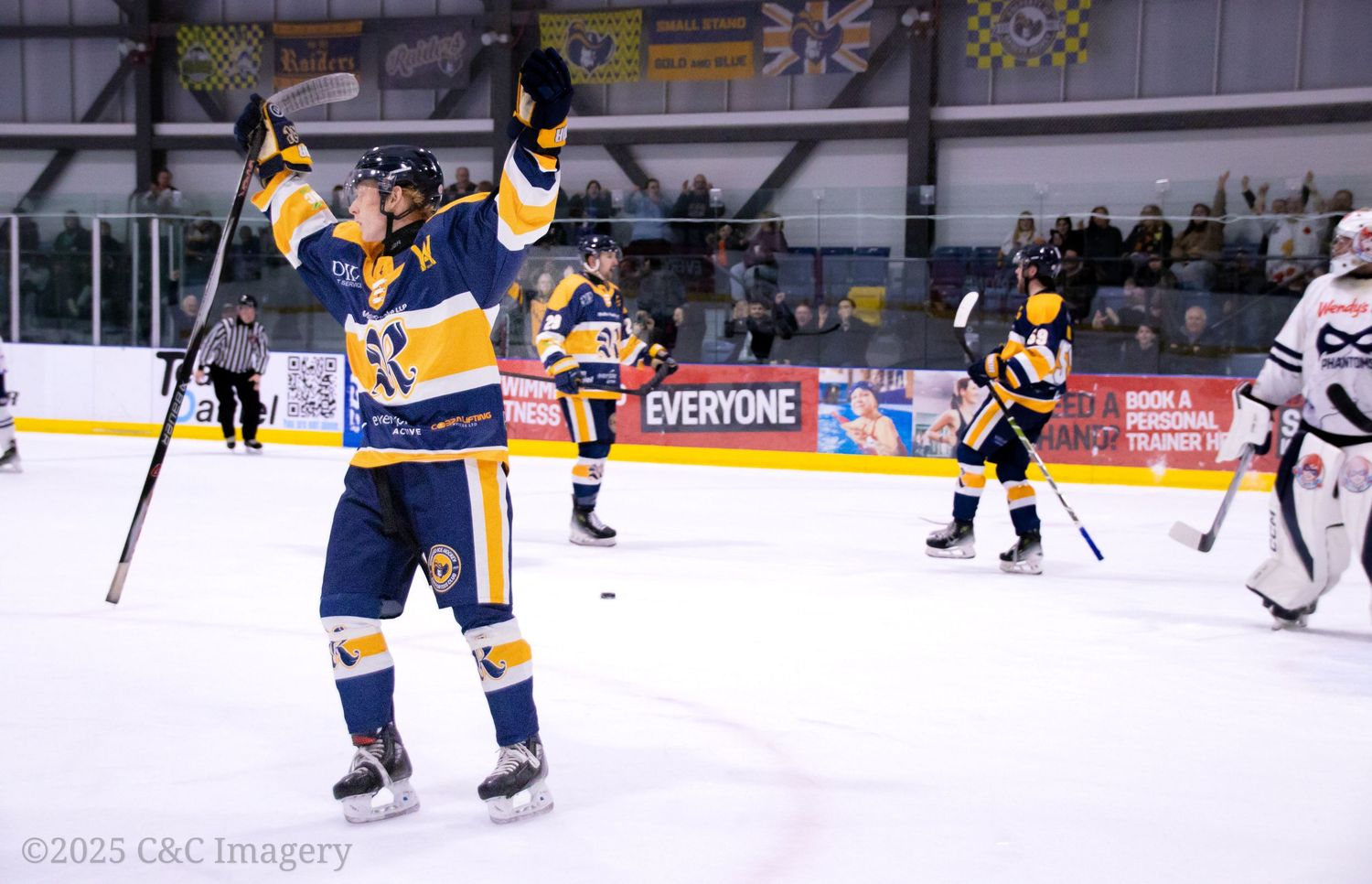 Hockey players in blue and yellow uniforms compete during an ice hockey match at an indoor arena.