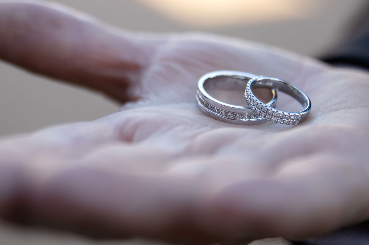 Two silver wedding rings with diamonds resting on an open palm in soft focus.