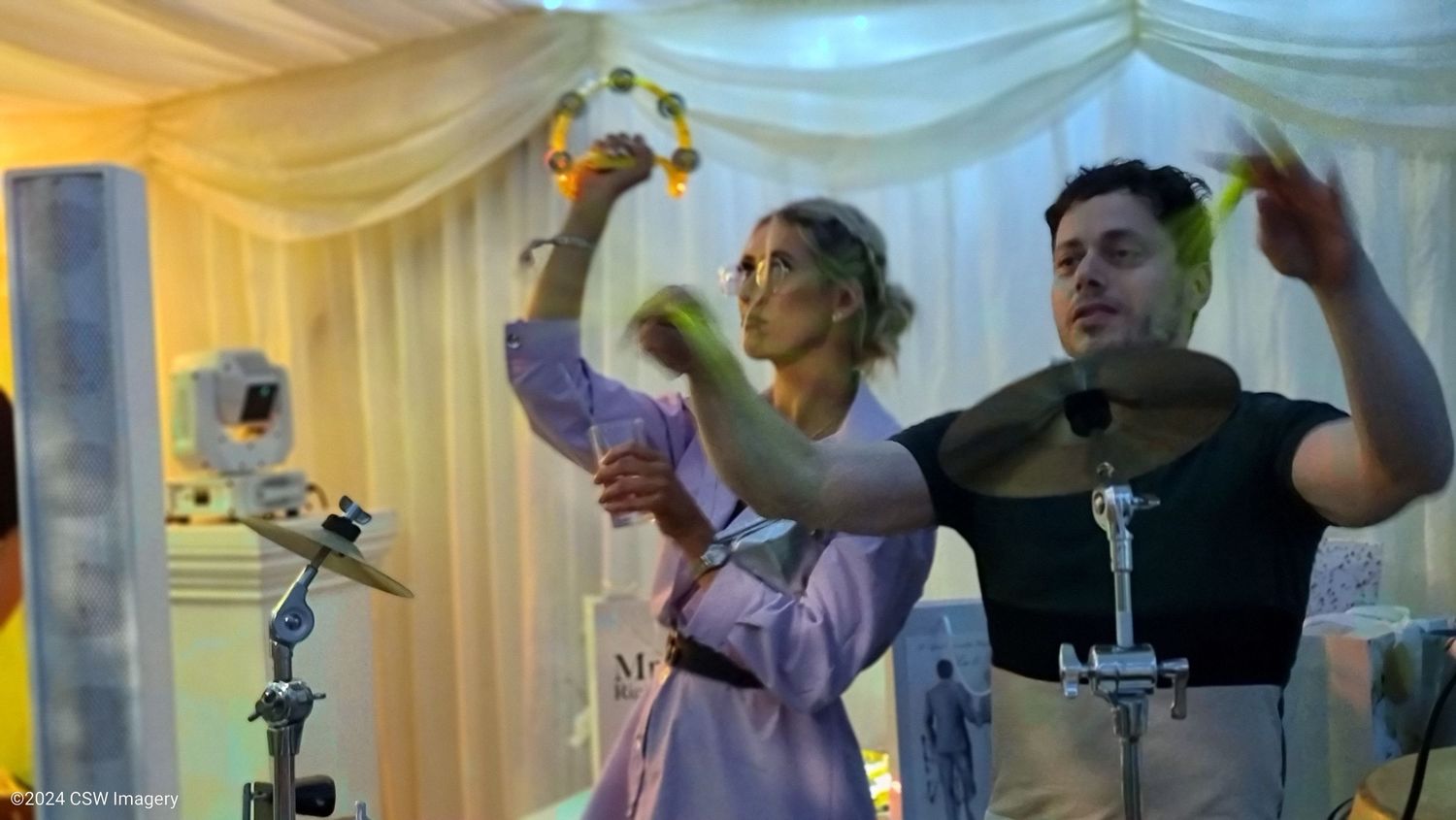 Wedding guests dancing and celebrating at a lively reception with white draped decor.