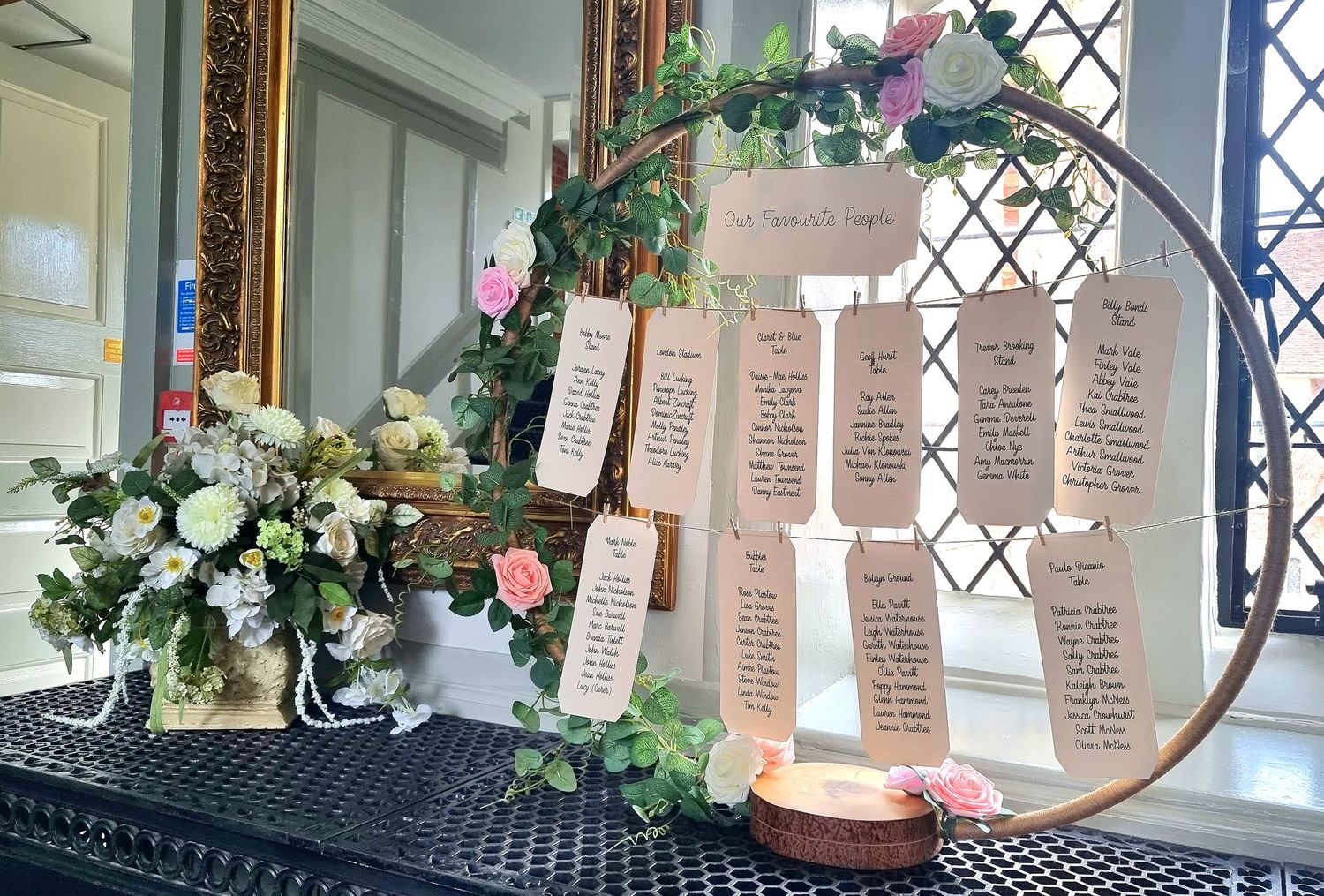 Elegant wedding seating chart display with floral arrangements and vintage decor near leaded glass windows.