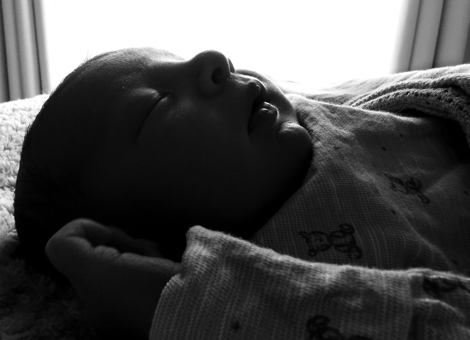 Black and white photo of a peaceful newborn baby lying on its back, wrapped in a soft blanket.