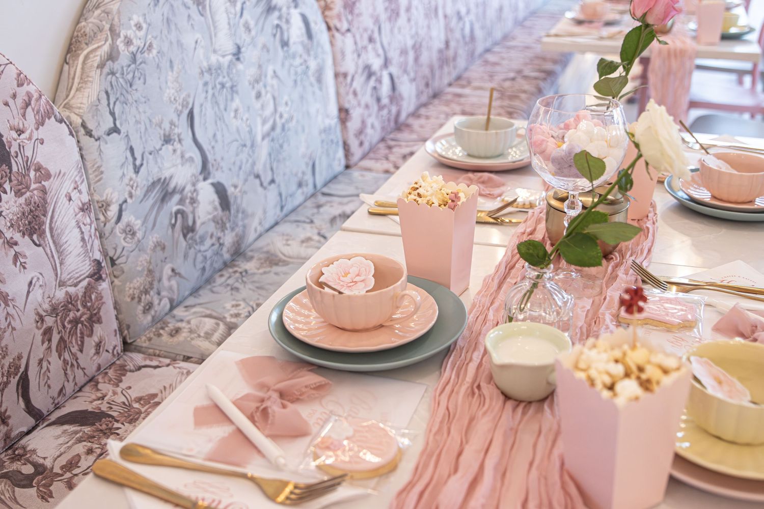 Elegant pink baby shower table setting with gold cutlery, pink tableware, floral centerpieces, and pastel decorations.