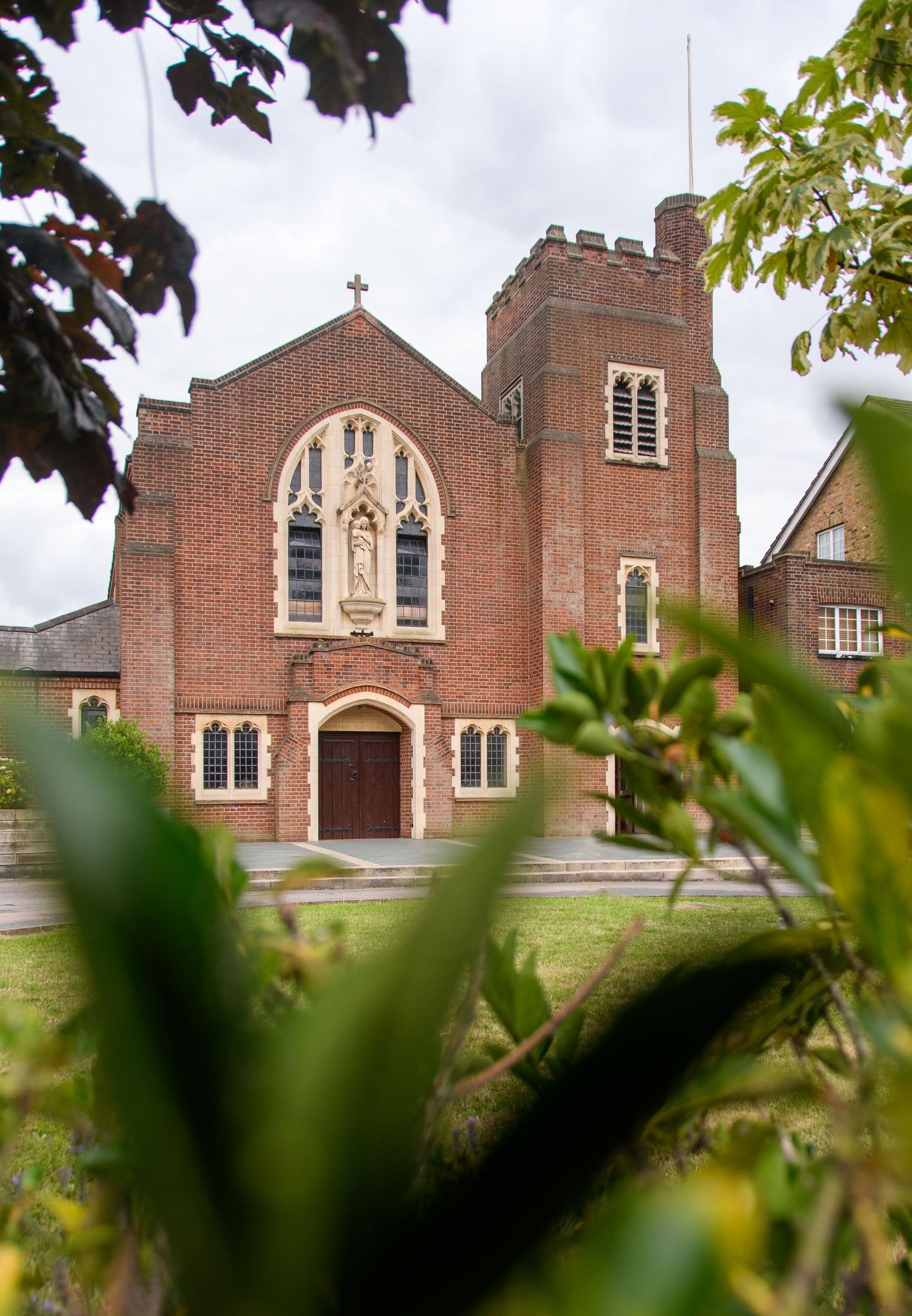 Brick church exterior with gothic arched windows and tower photographed through foliage.