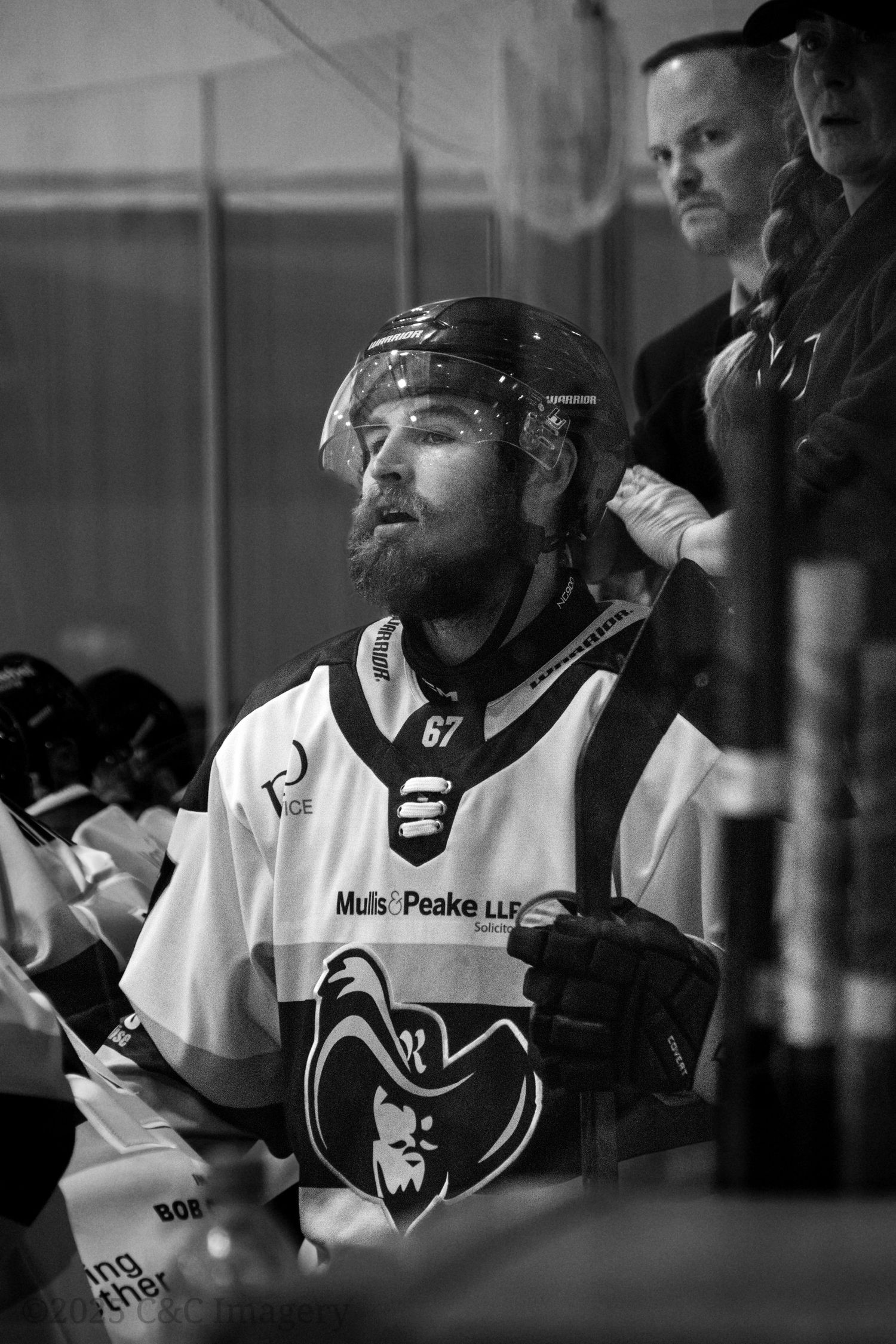 Hockey player in white jersey sits on bench during game in black and white photography.