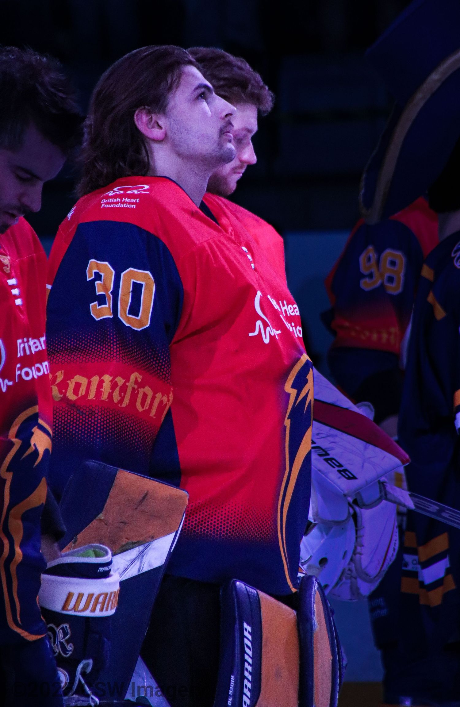Players in red jerseys line up during a hockey game under dramatic lighting.
