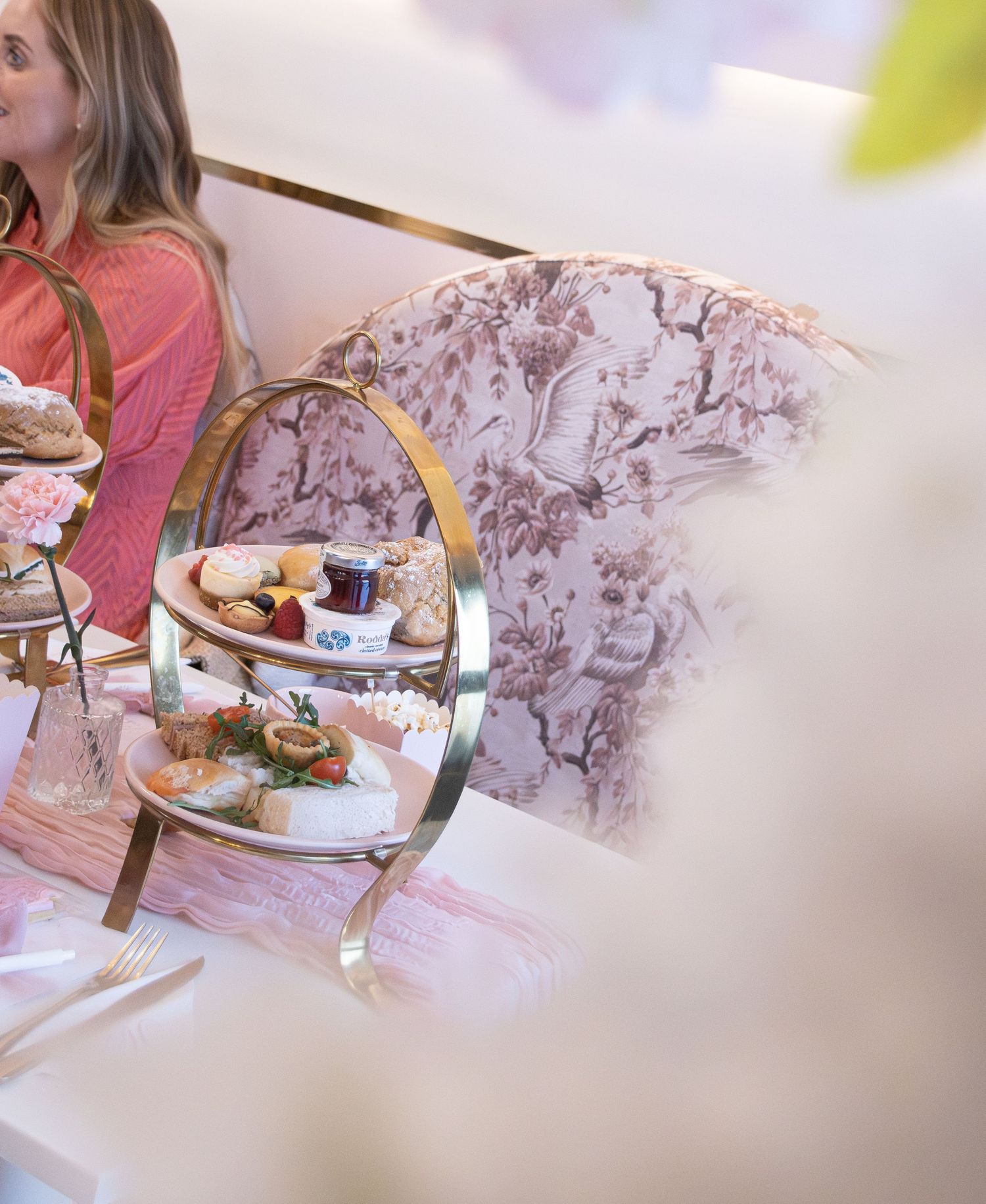 Elegant afternoon tea service on a tiered stand with sandwiches and pastries in a floral-decorated tearoom.