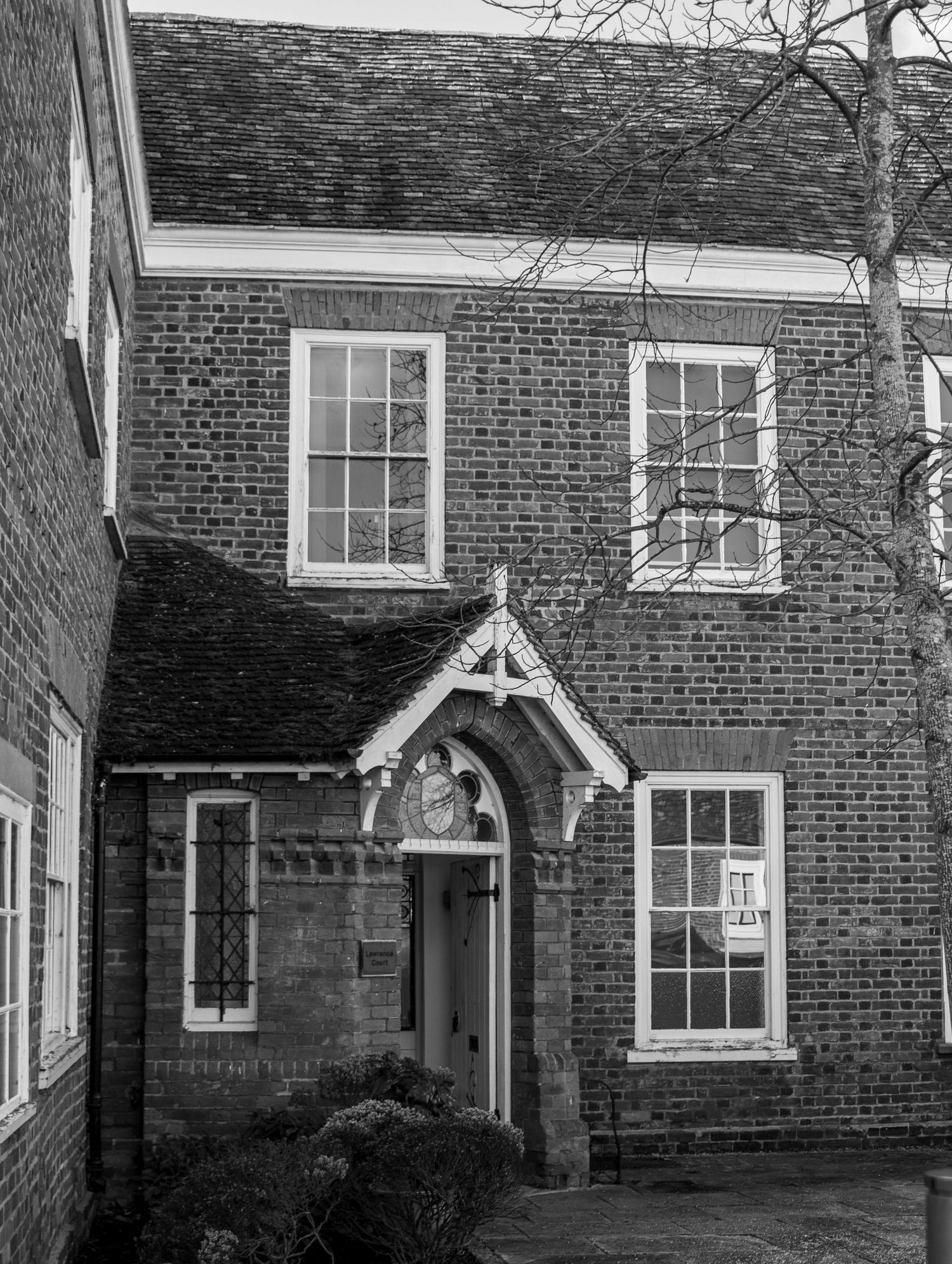 Black and white photograph of a traditional brick house with ornate gabled entryways and multiple windows.