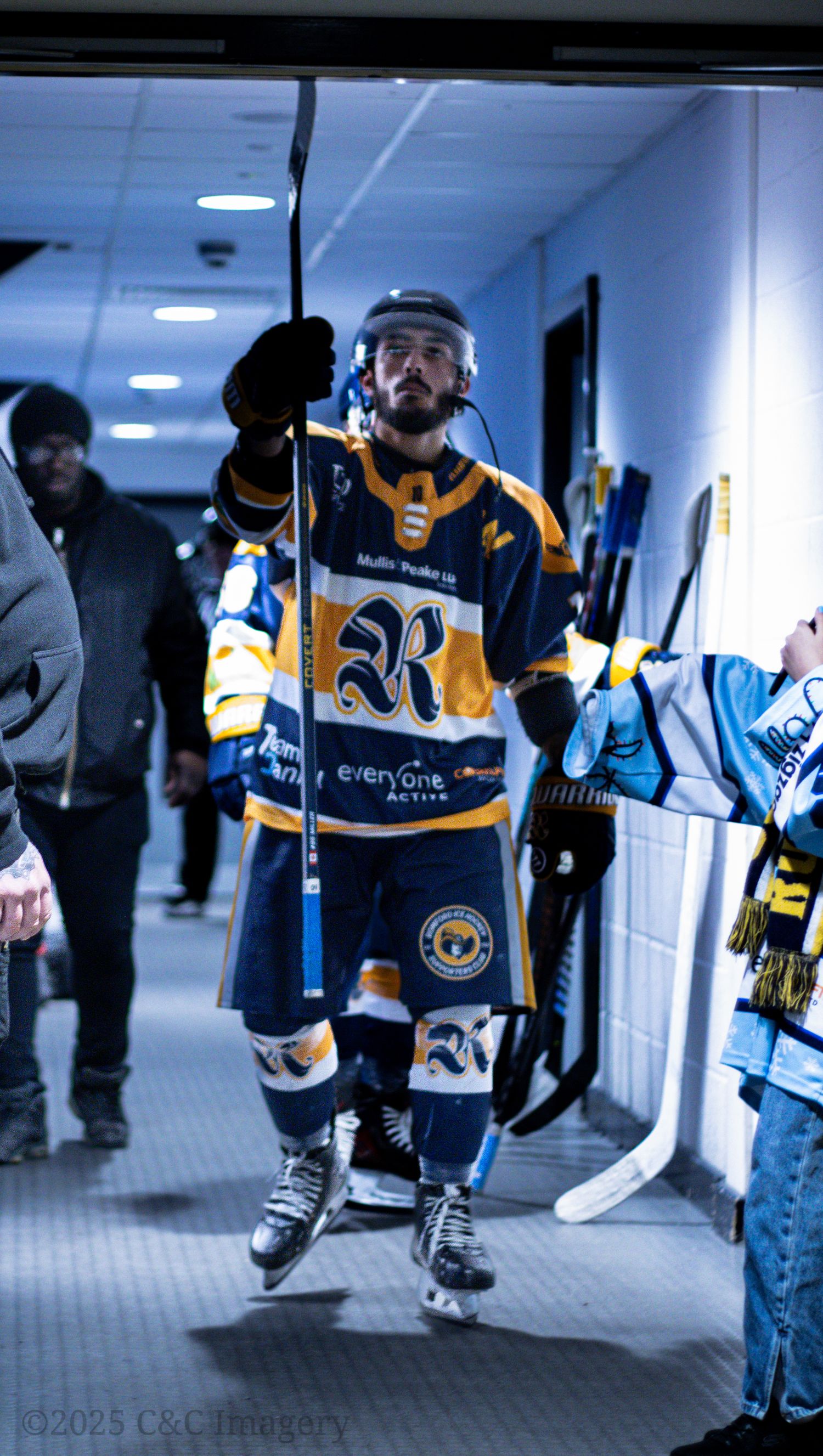 Hockey players in blue and yellow jerseys walk through an indoor hallway before a game.
