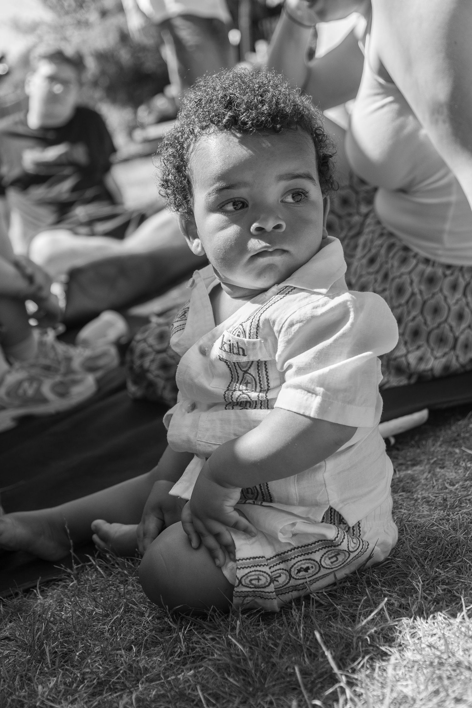 Black and white portrait of a young toddler sitting on grass outdoors.