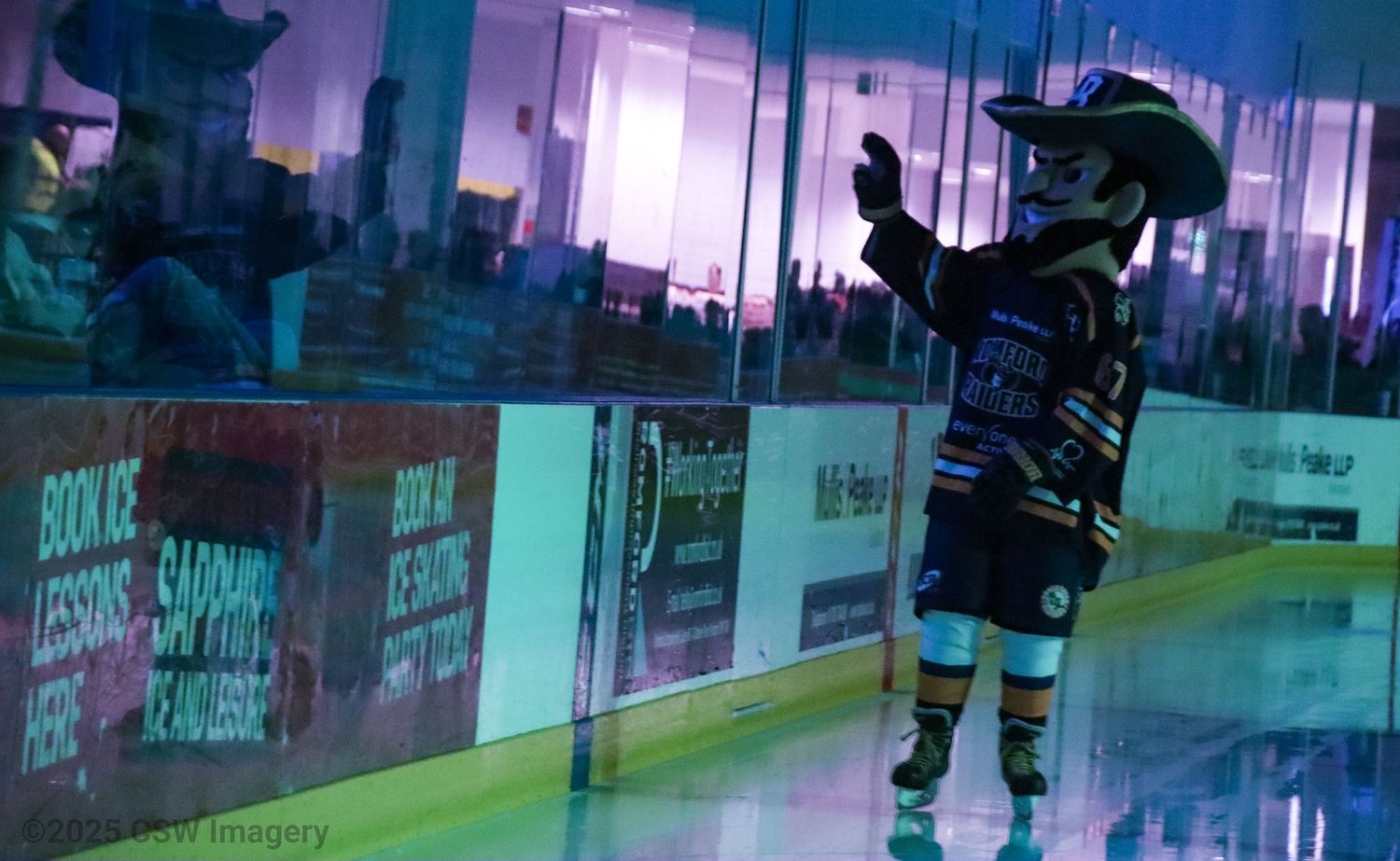 Purple and teal lighting illuminates an empty hockey rink with advertisements along the boards.