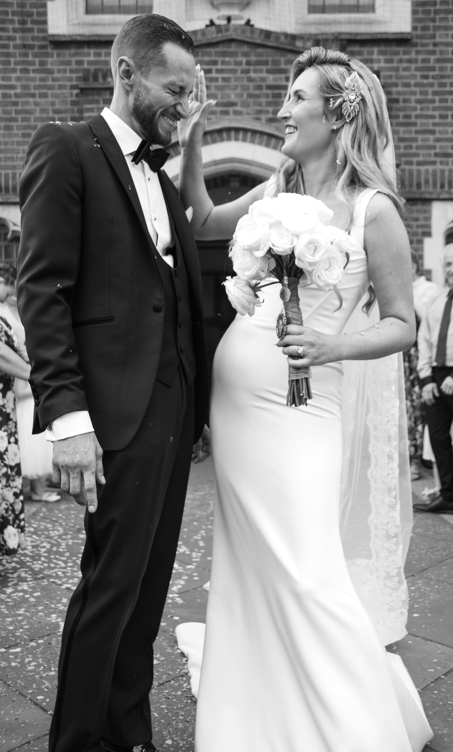 Black and white wedding portrait captured outside a brick church building.