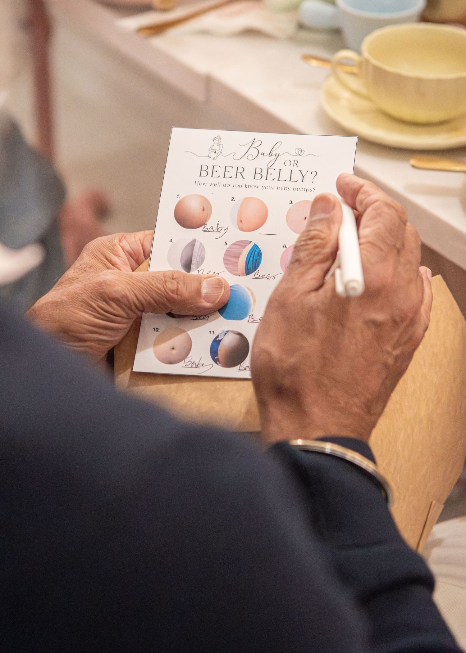 Person filling out a Baby or Beer Belly gender reveal game card with a white pen at a baby shower.