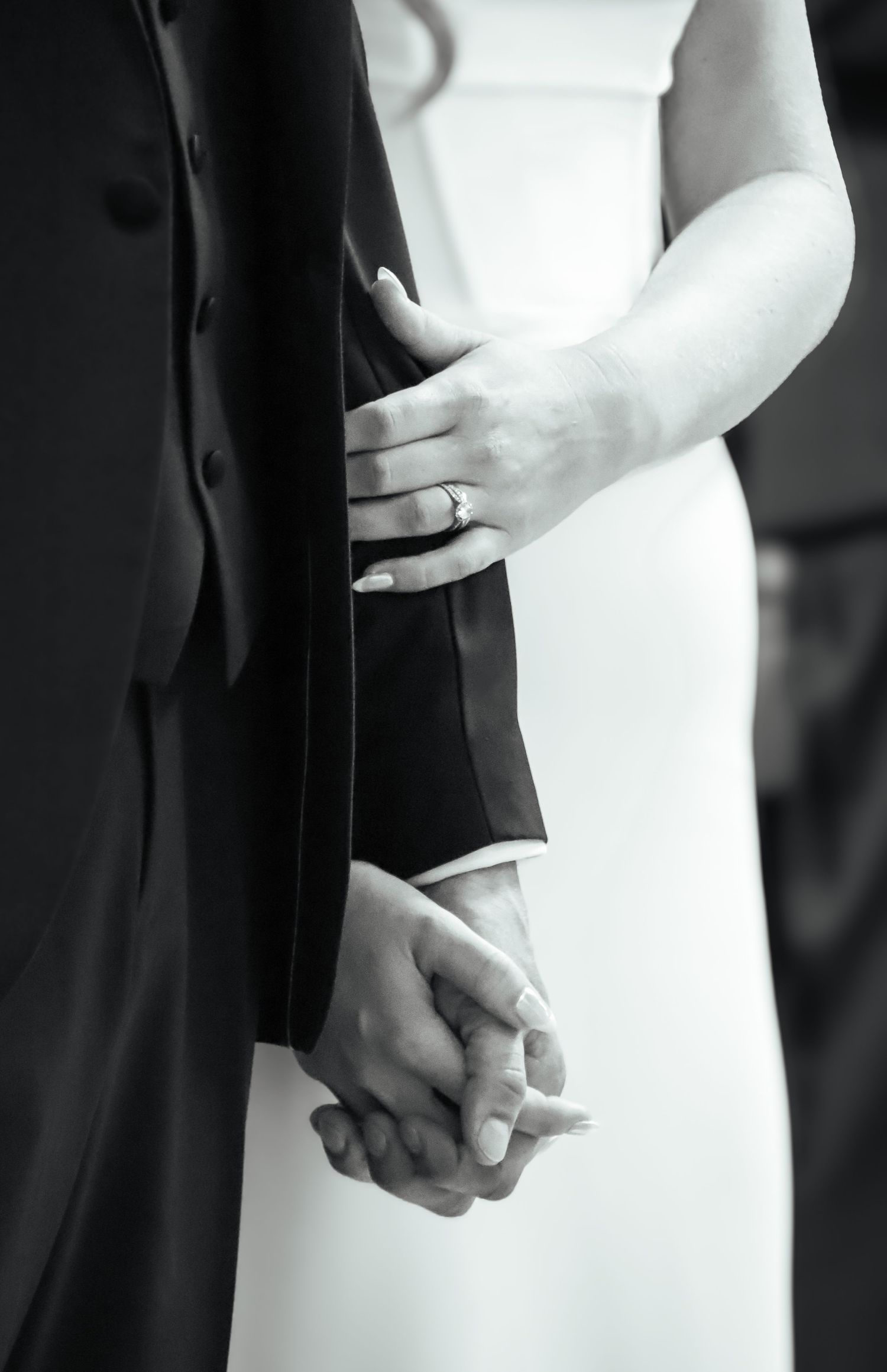 Artistic black and white detail shots of a bride and groom holding hands during wedding ceremony.
