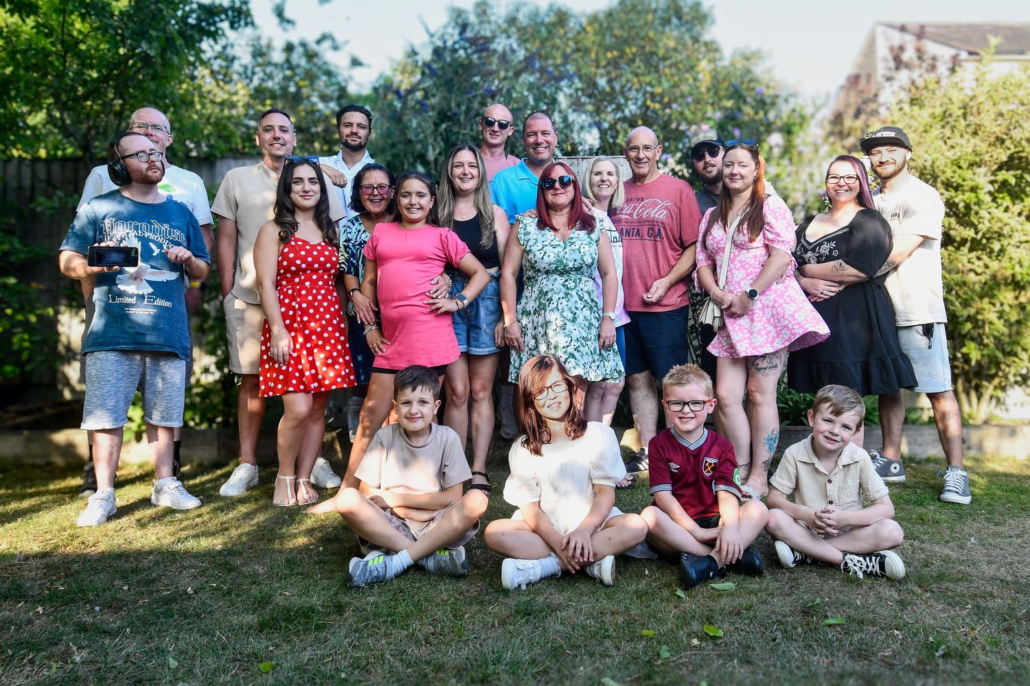 Large group of people gathered outdoors for a casual photo in a sunny garden setting.