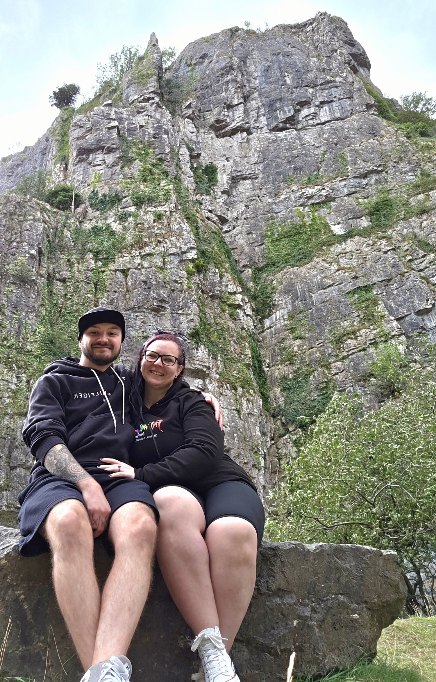 Couple sitting on large rocks with dramatic cliff face in background.