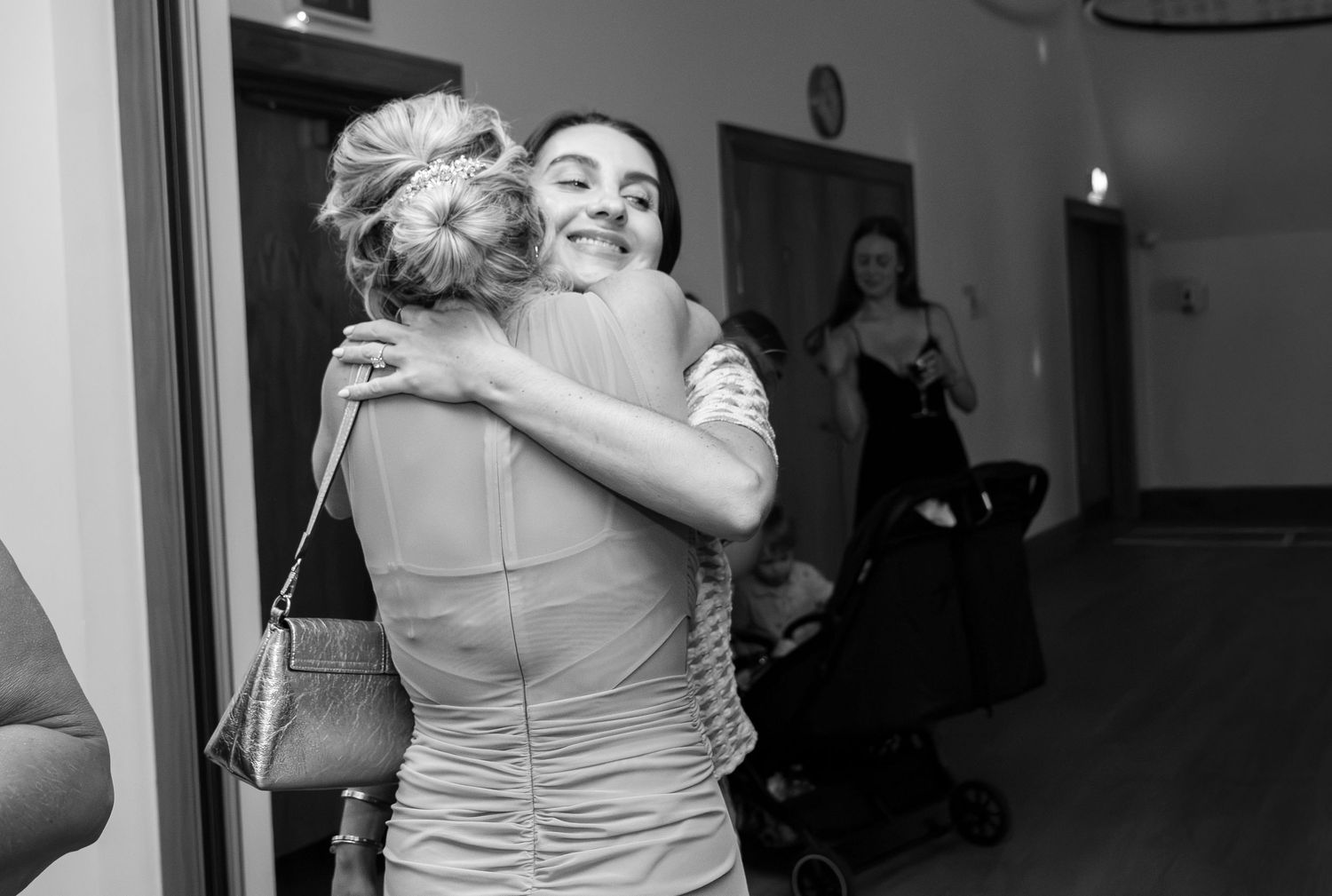 Two women share a warm embrace at a wedding reception in this black and white candid photography moment.