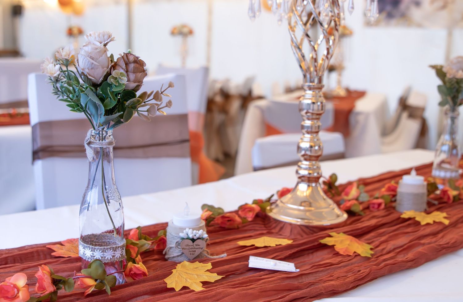 Fall table decor with orange and red autumn leaves arranged on a burgundy table runner with crystal candlesticks.